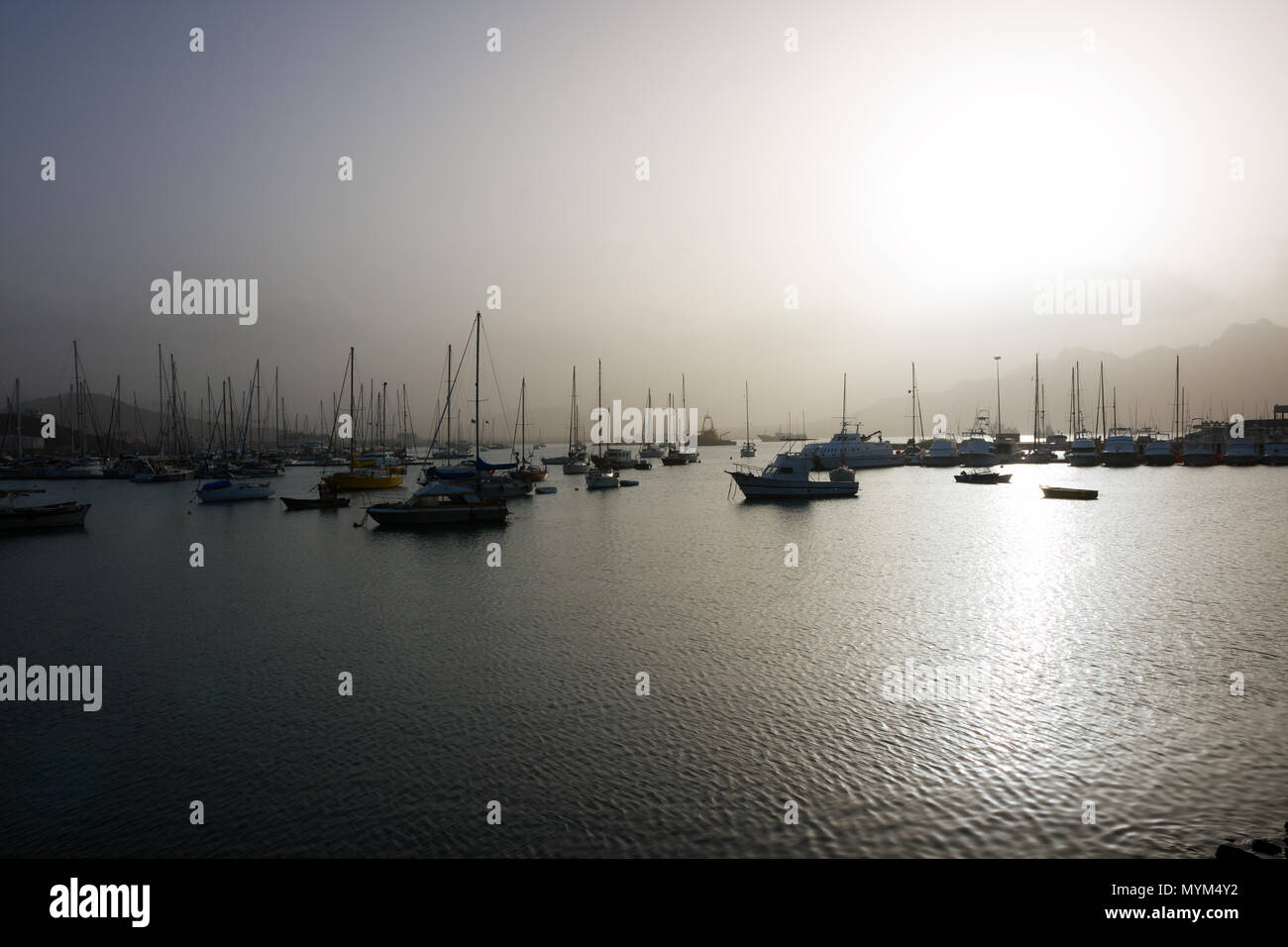 MINDELO, CAPE VERDE - DECEMBER 07, 2015: Boats and yachts in port of Sao Vicente island in bright light of the misty sunset Stock Photo