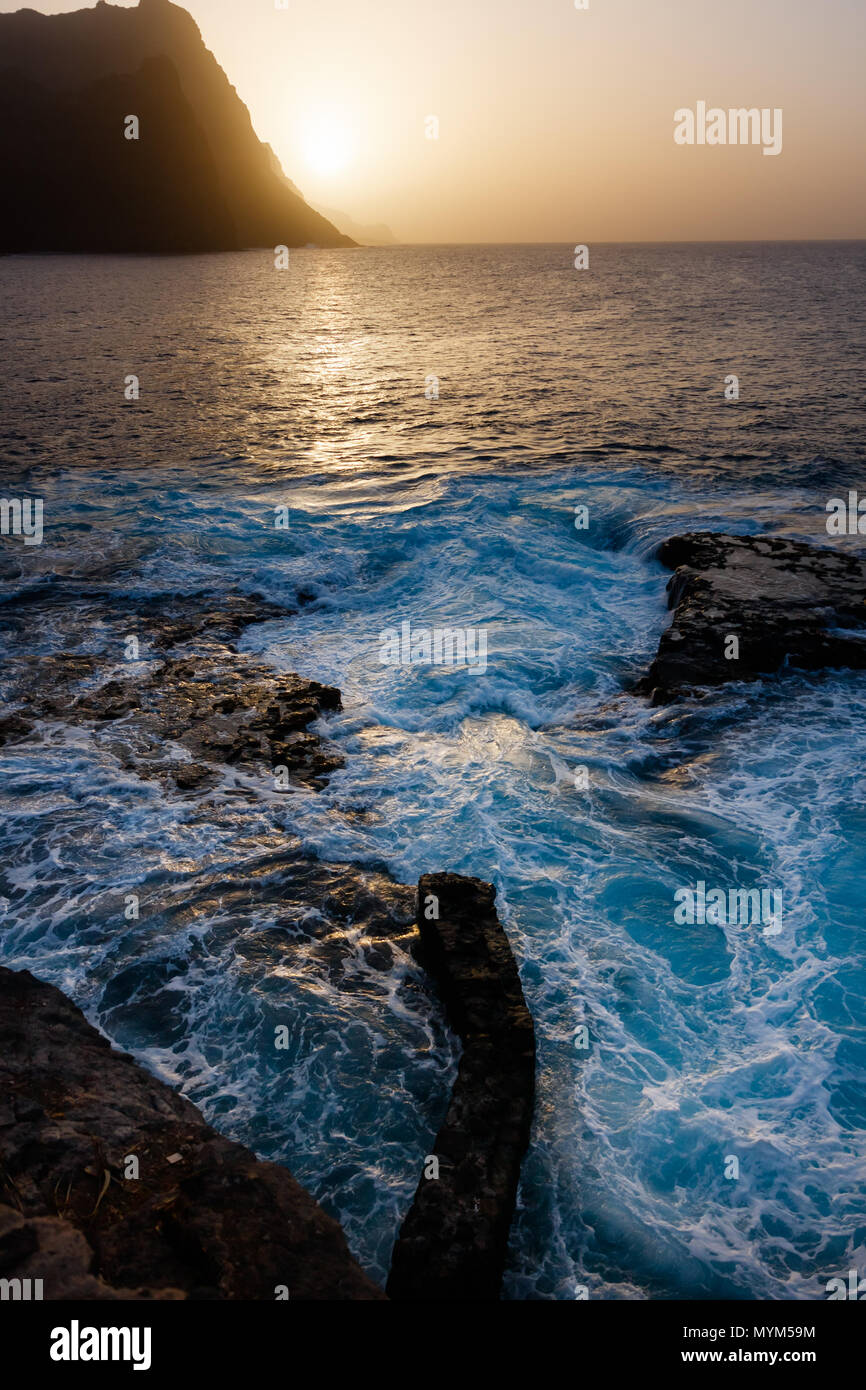 Dusty sunset and turbulent waves at the rocky beach of Santo Antao Island Stock Photo