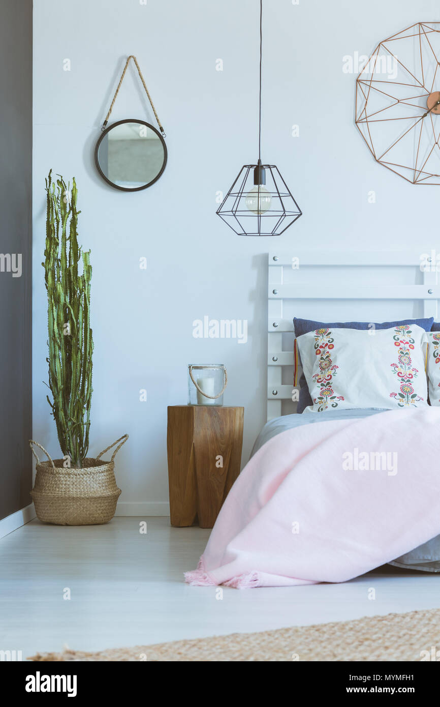 White bedroom with industrial clock, lamp, decorative folk pillows, cactus Stock Photo