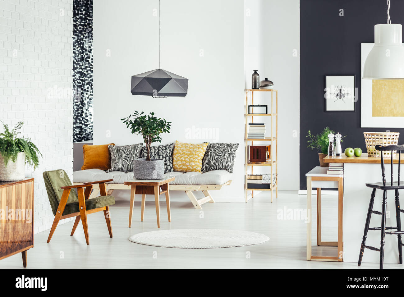 Small tree in material pot on wood table next to vintage green chair in room with patterned pillows on sofa Stock Photo