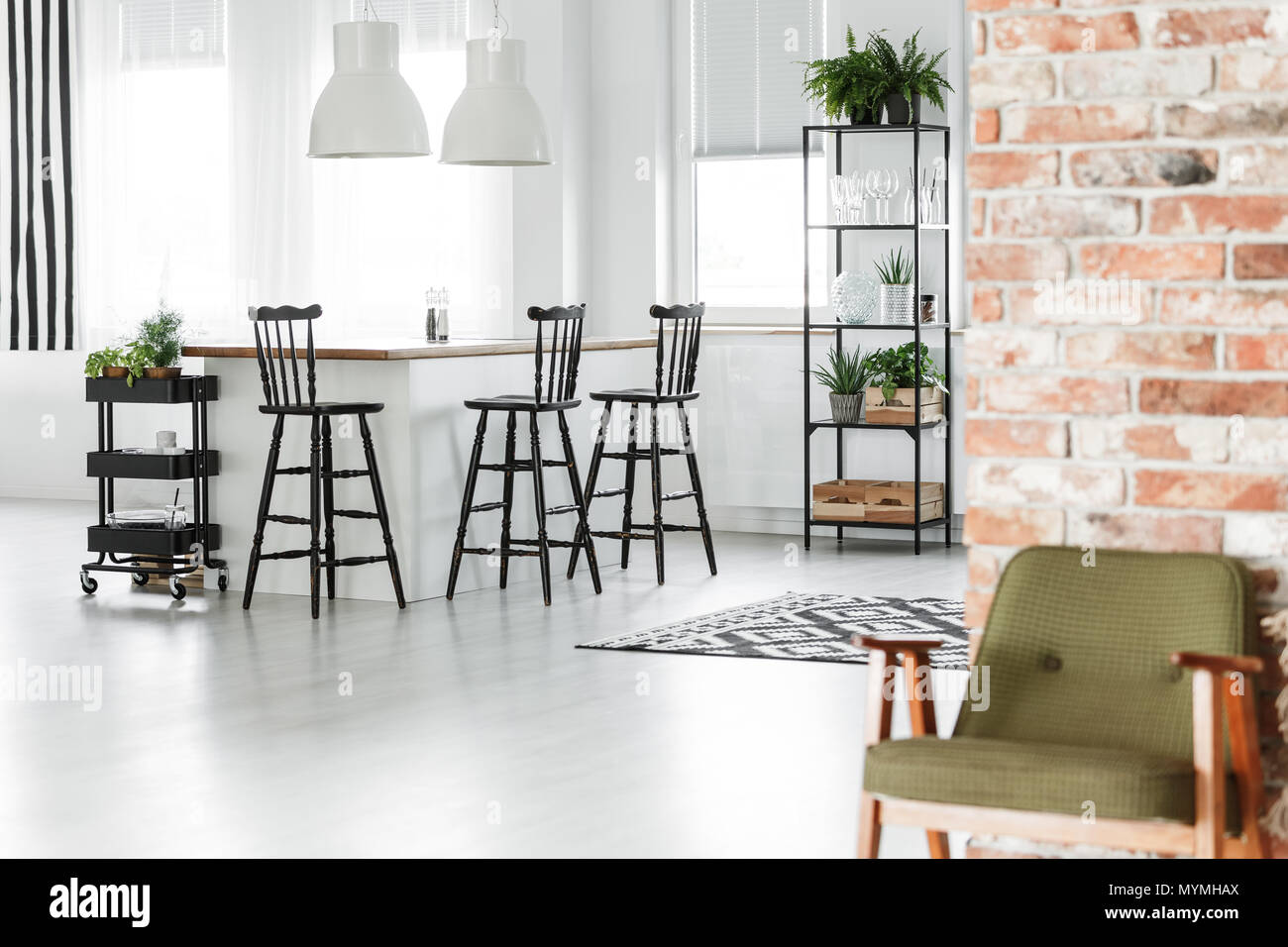 Retro green chair against red brick wall in room with black bar stools and kitchen island Stock Photo