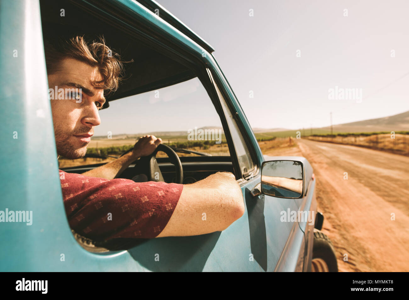 Close up of a man looking out of the window while driving a car. Man driving car on a mud track. Stock Photo