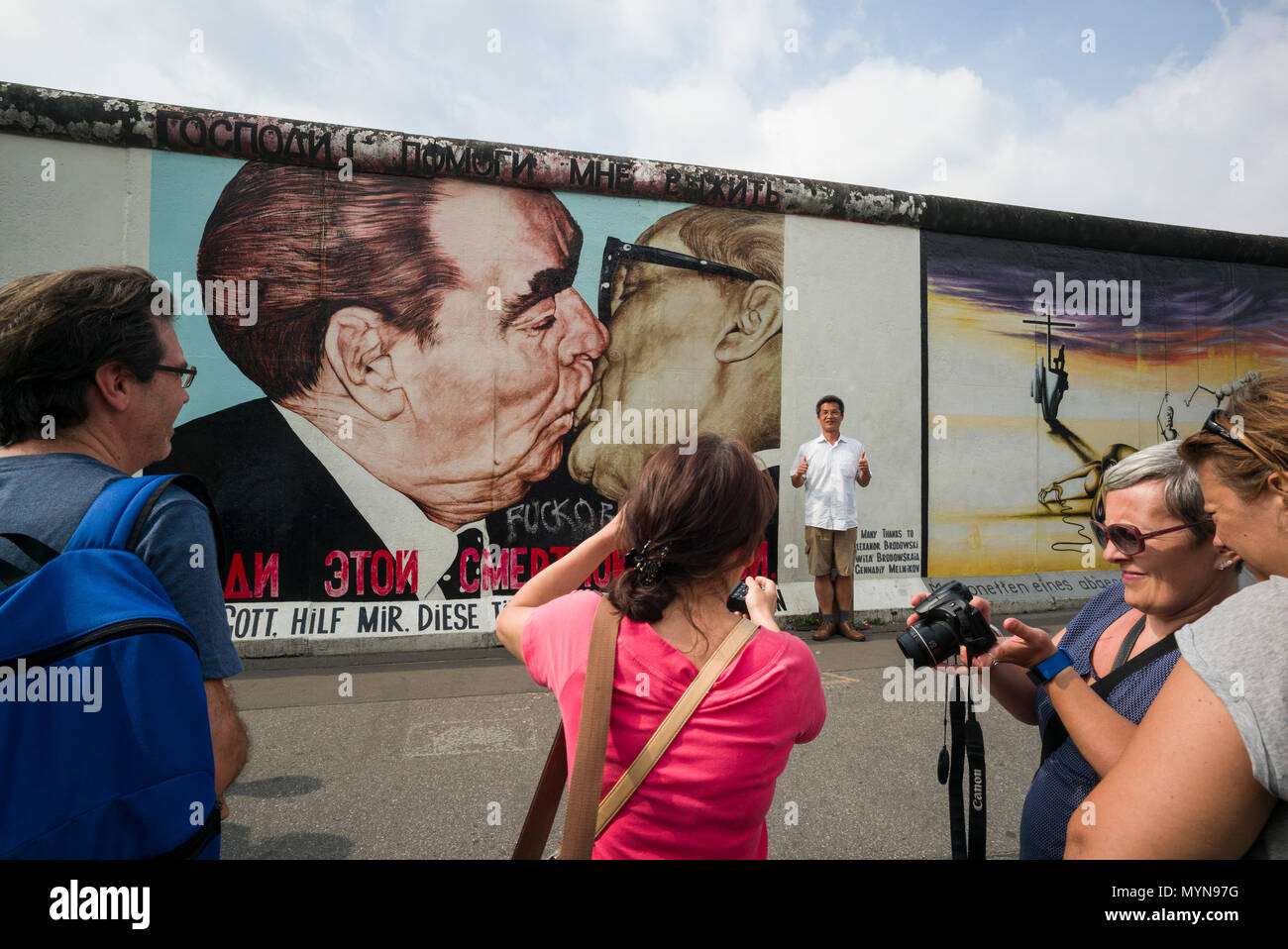 Berlin. Germany. Tourists pose for photos infront of one of the remaining sections of the Berlin Wall at the East Side Gallery.   Tourists pose for ph Stock Photo