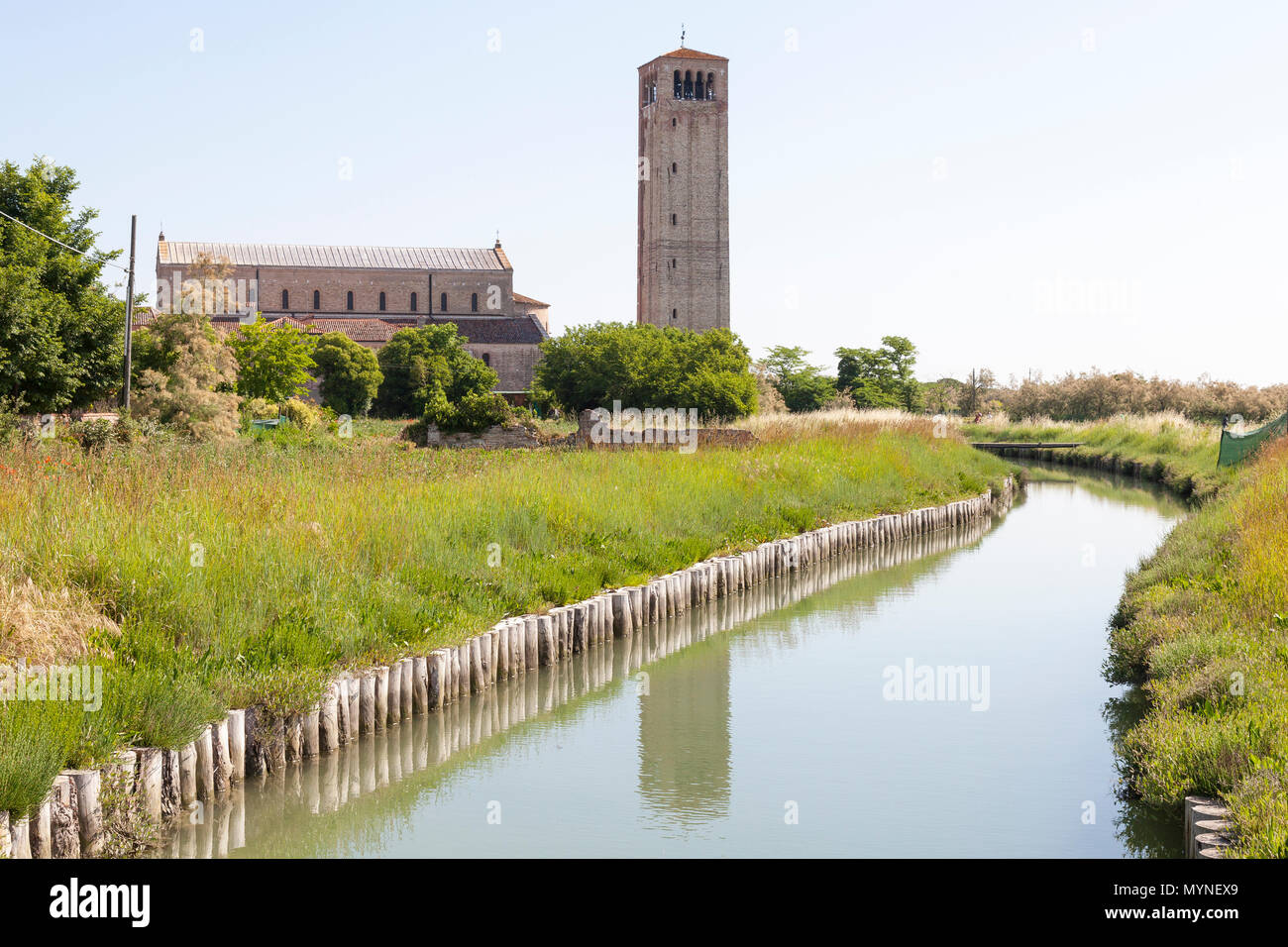 Basilica di Santa Maria Assunta at sunrise, Torcello Island, Venice, Veneto, Italy with the bell tower or campanile reflected in the canal. Scenic lan Stock Photo