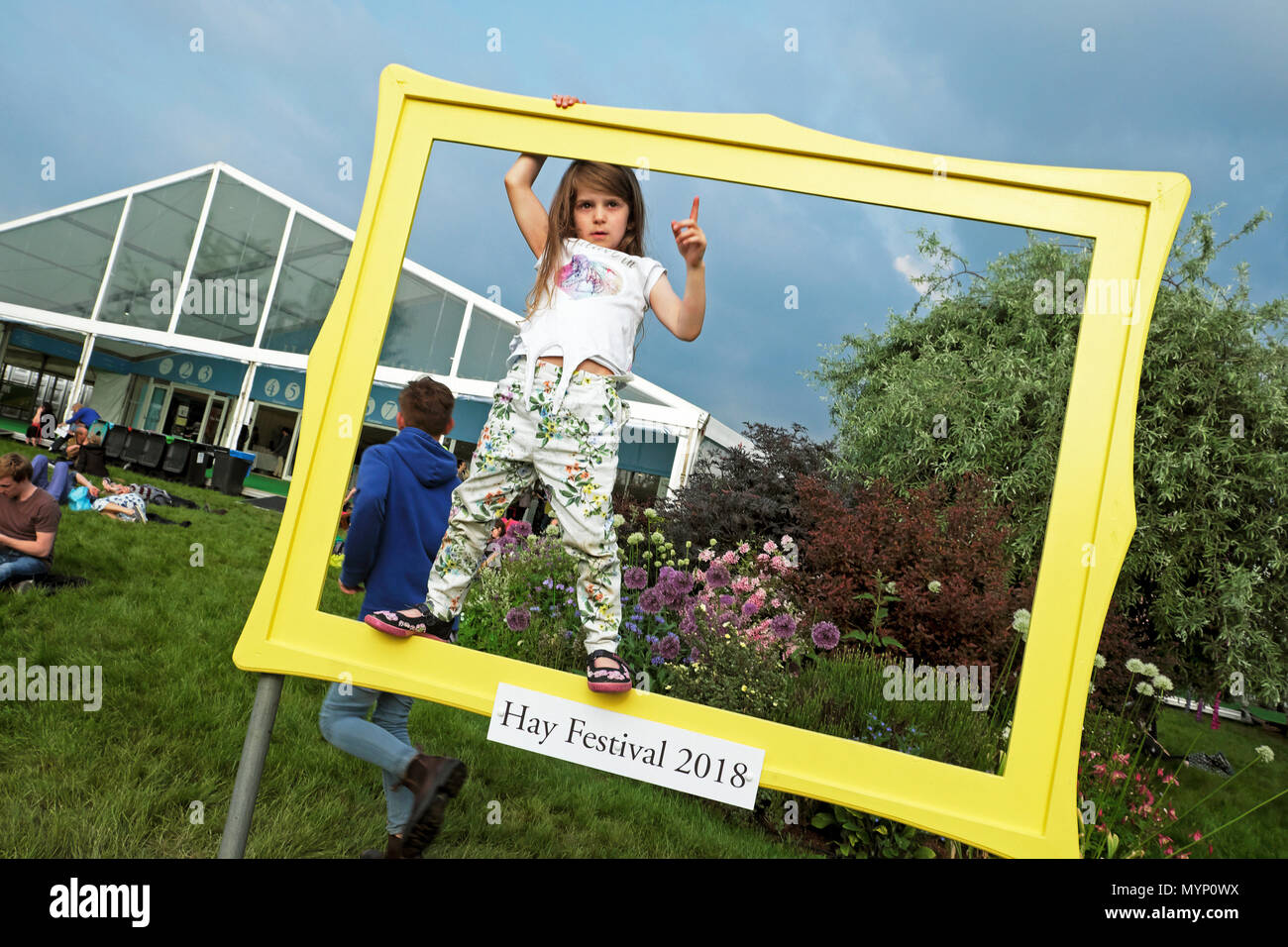 Child playing on the site standing in a picture frame in the garden outside the bookshop at Hay Book Festival 2018 in Hay-on-Wye Wales UK KATHY DEWITT Stock Photo