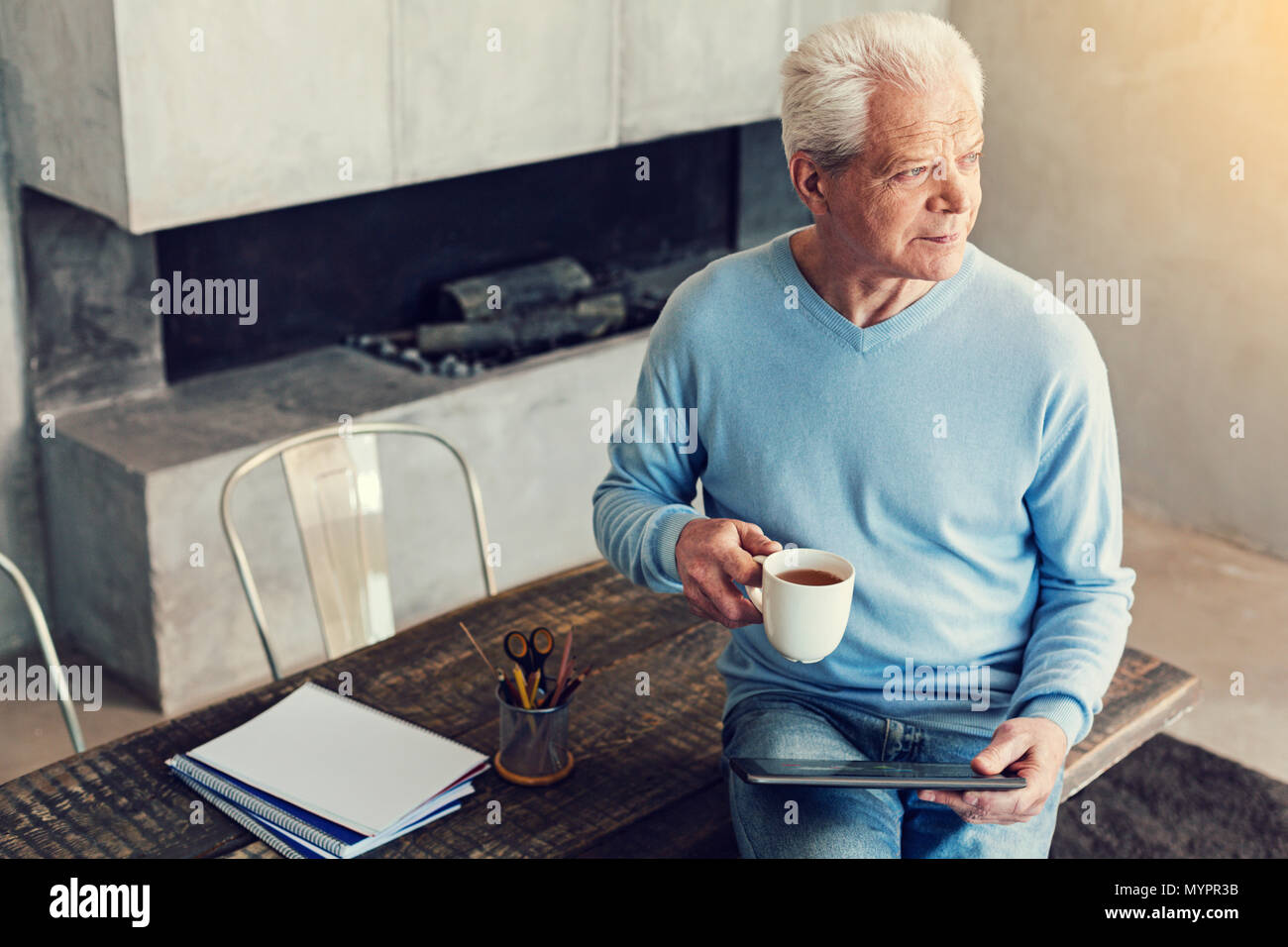 Thoughtful senior man sitting with a cup and a tablet Stock Photo