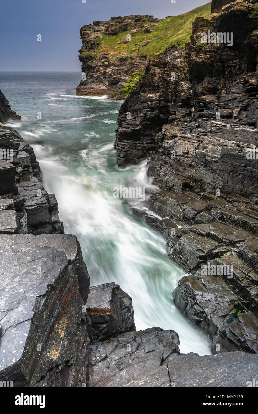 Waves rush into one of the inlets at Bossiney Cove in North Cornwall at high tide. Stock Photo