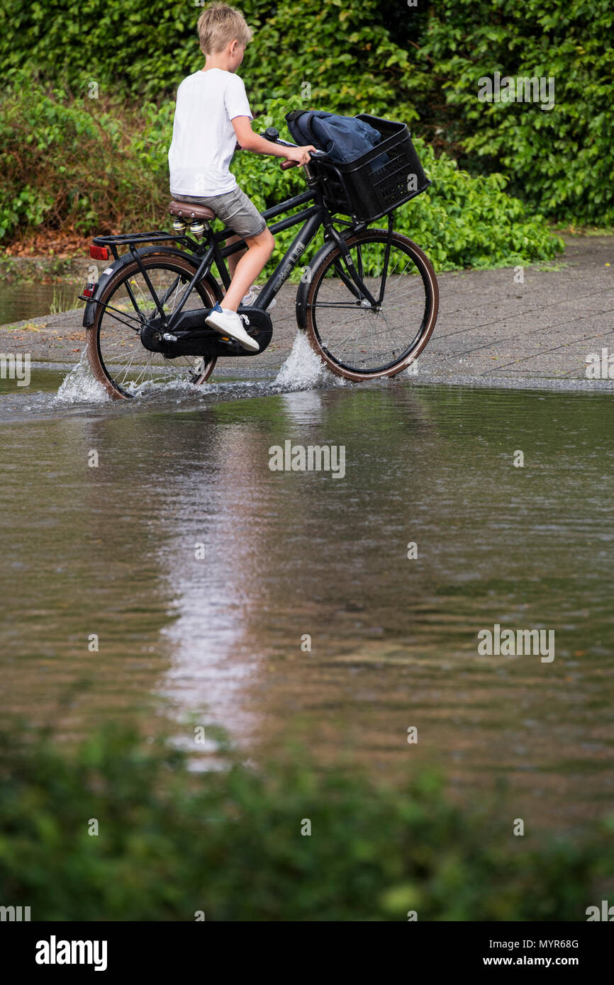 Young boy riding a bike through flood water in a street after