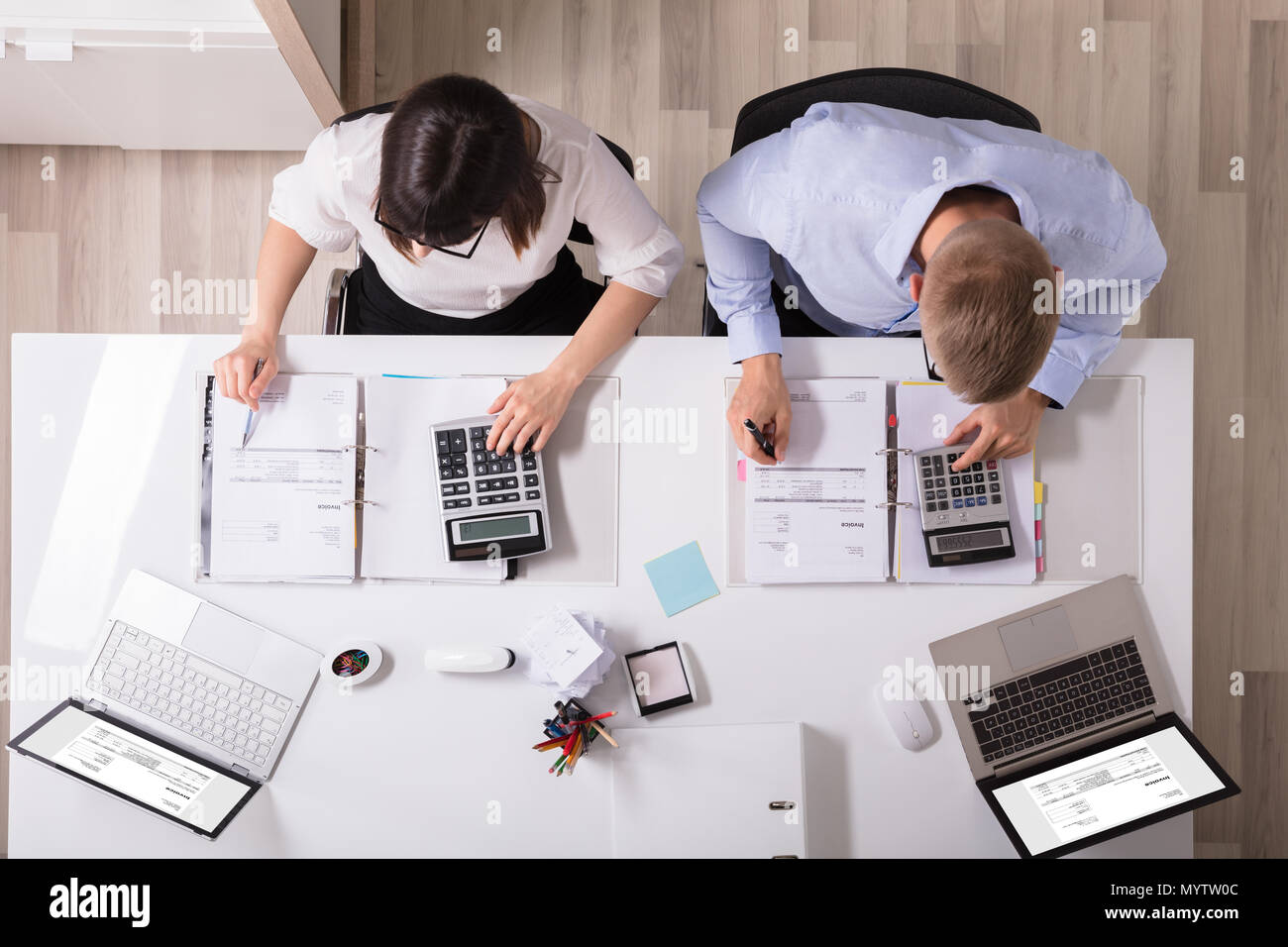 Two Young Businesspeople Calculating Invoice With Calculator Stock Photo