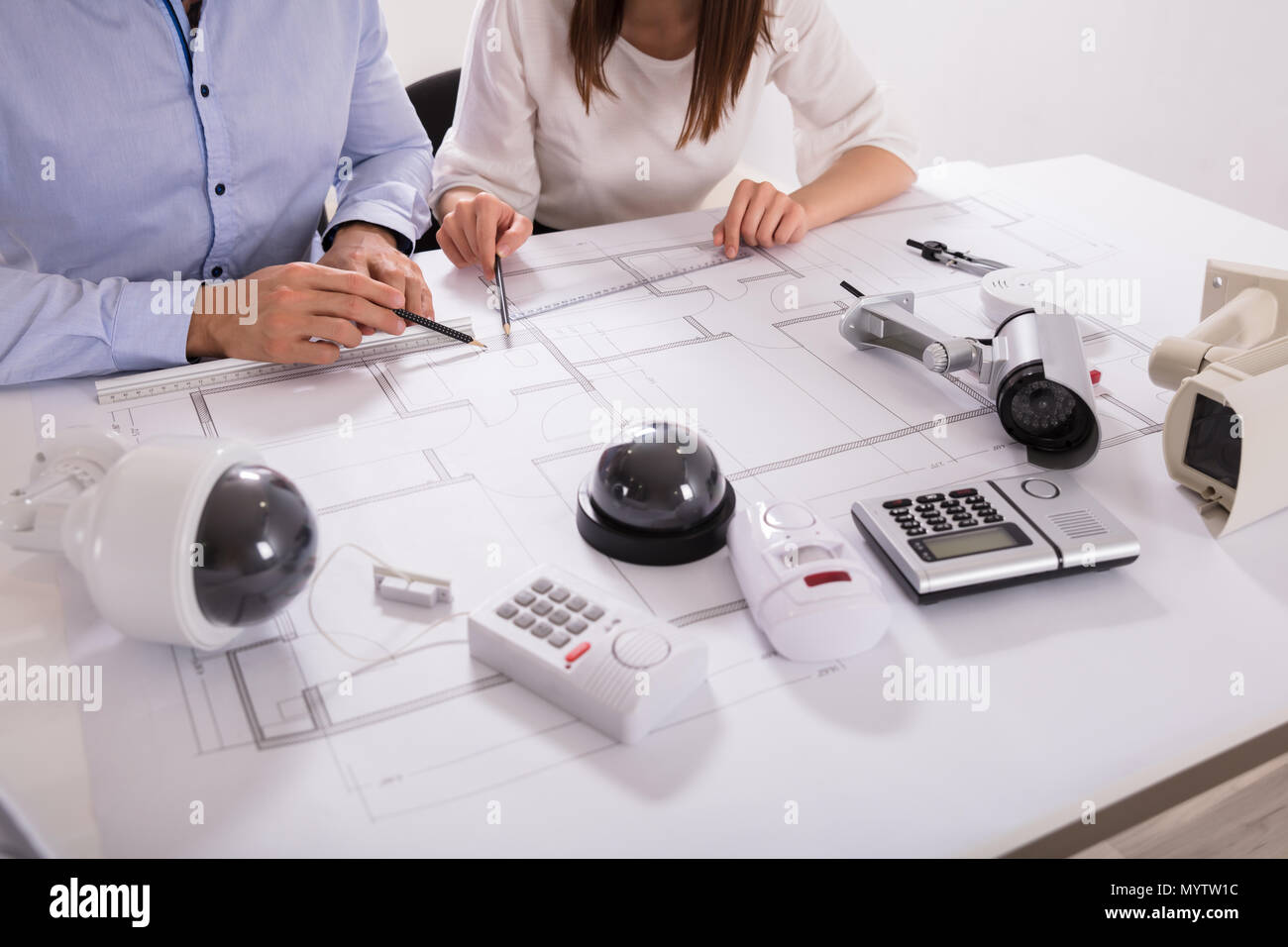 Various Security Equipments In Front Of Two Architects Planning Project On Blueprint Stock Photo