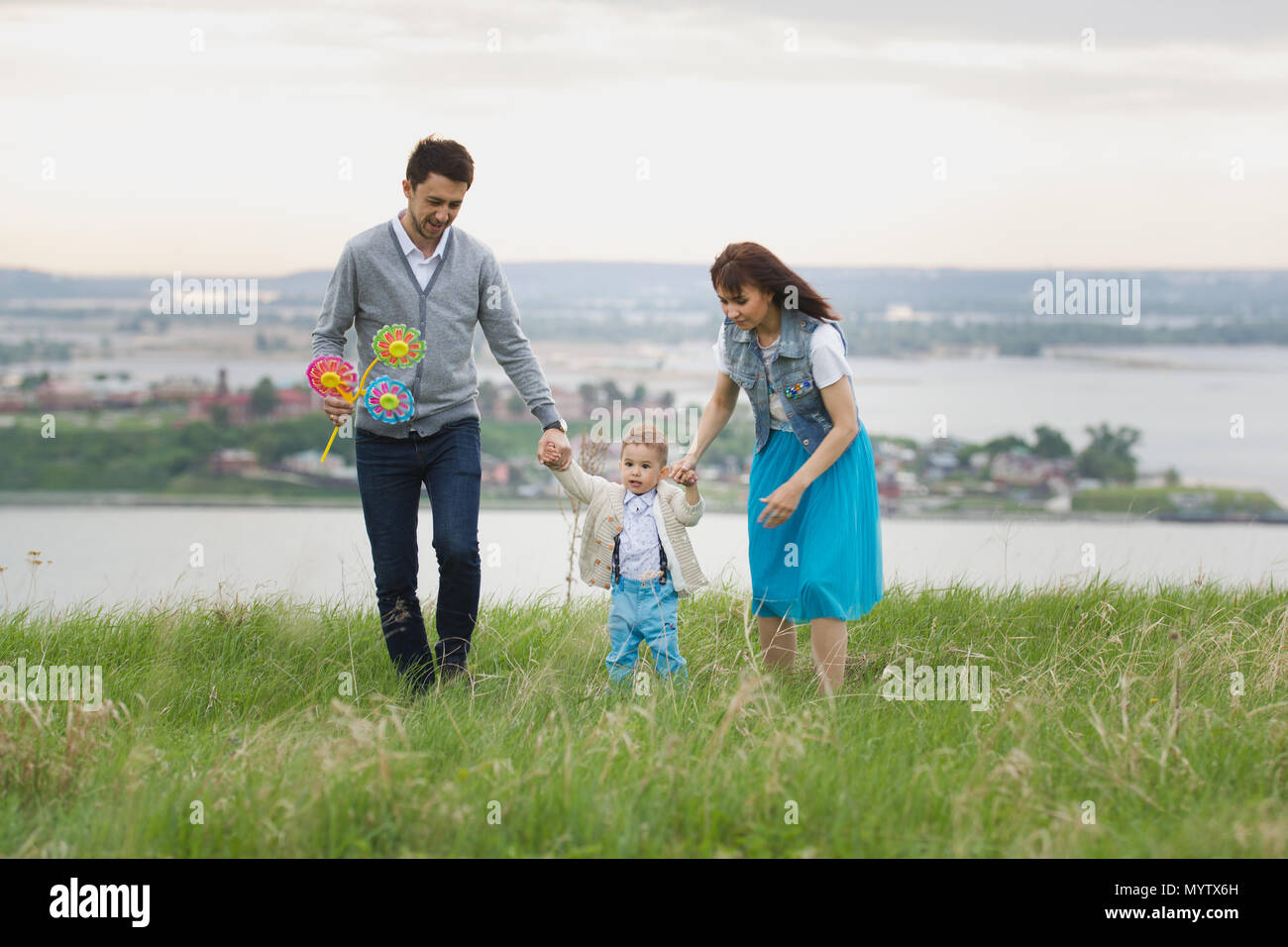 Parents hold their son's hands and raise, the baby jumps, cloudy Stock Photo