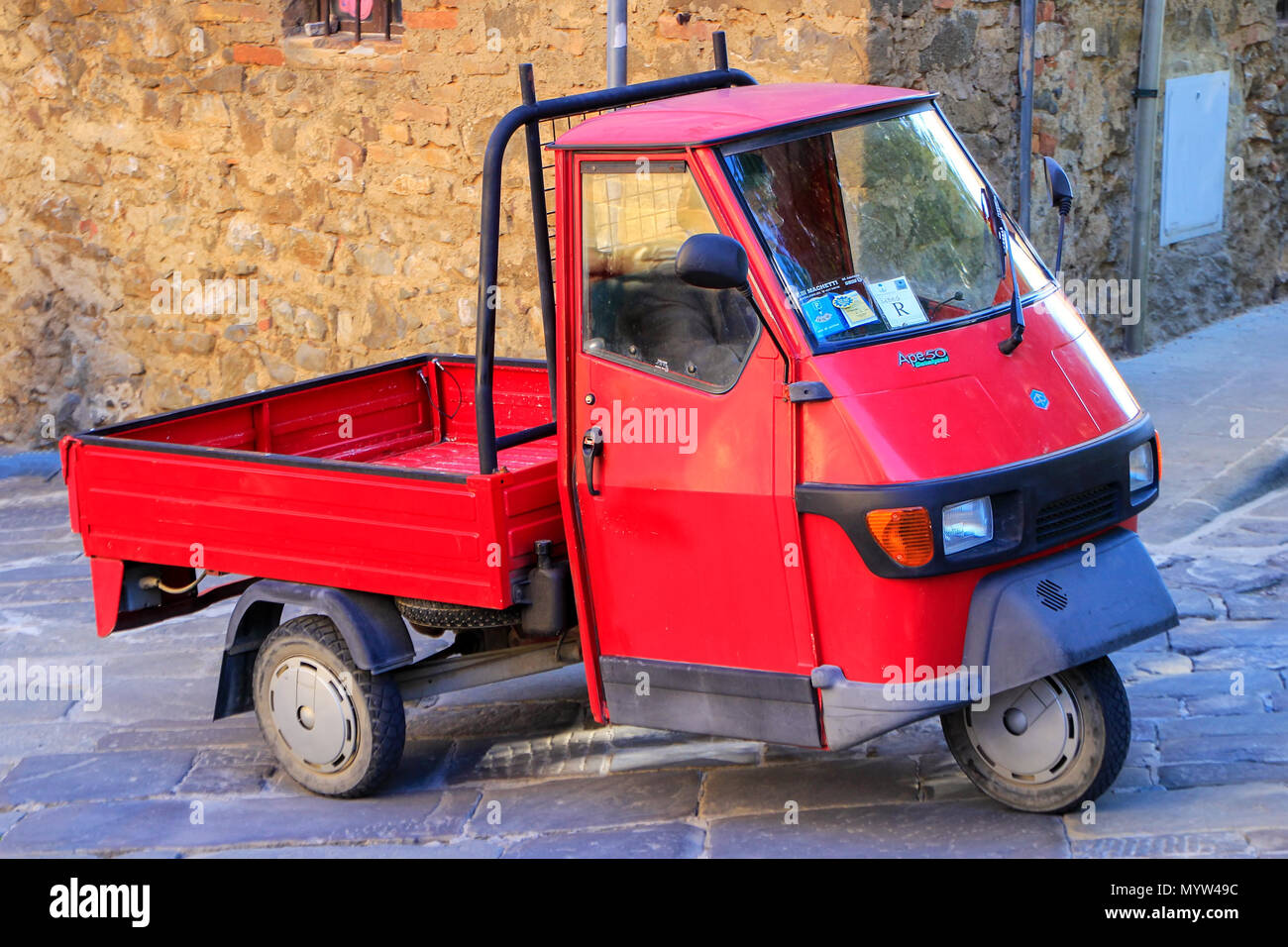 Red Piaggio Ape 50 in the street of Montalcino town, Val d'Orcia, Tuscany, Italy. The vehicle is produced since 1948. Stock Photo