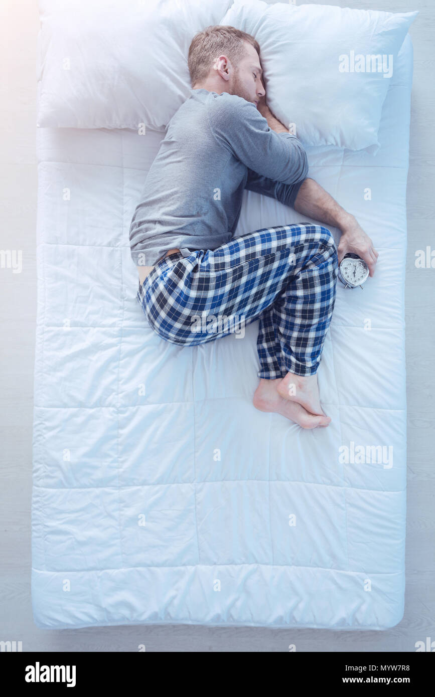 Man with alarm clock sleeping in fetal position Stock Photo