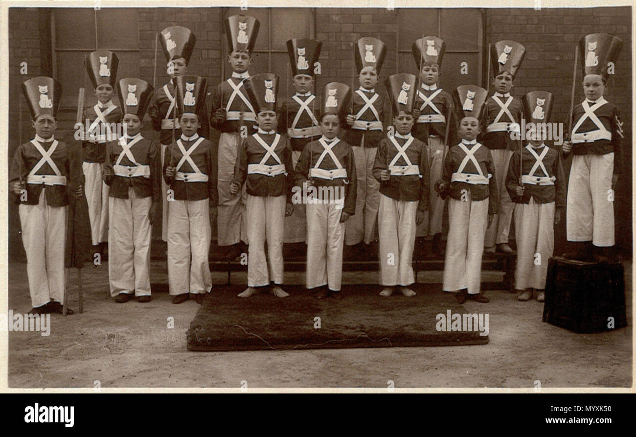 . Postcard group portrait of boys dressed as tin soldiers at or near Swindon, Wiltshire, England, 1920s or 30s. The photographer was Fred C. Palmer of Tower Studio, Herne Bay, Kent ca.1905-1916, and of 6 Cromwell Street, Swindon ca.1920-1936. He is believed to have died 1936-1939. Points of interest  The location is possibly outside a school, because a school form and coconut mat are in use (both used in school gymnastics at that time). The windows appear to be frosted. The boy on the left is holding a rolled-up banner, and two of the cat-cutouts have gone awry. Could this be part of a Puss-in Stock Photo