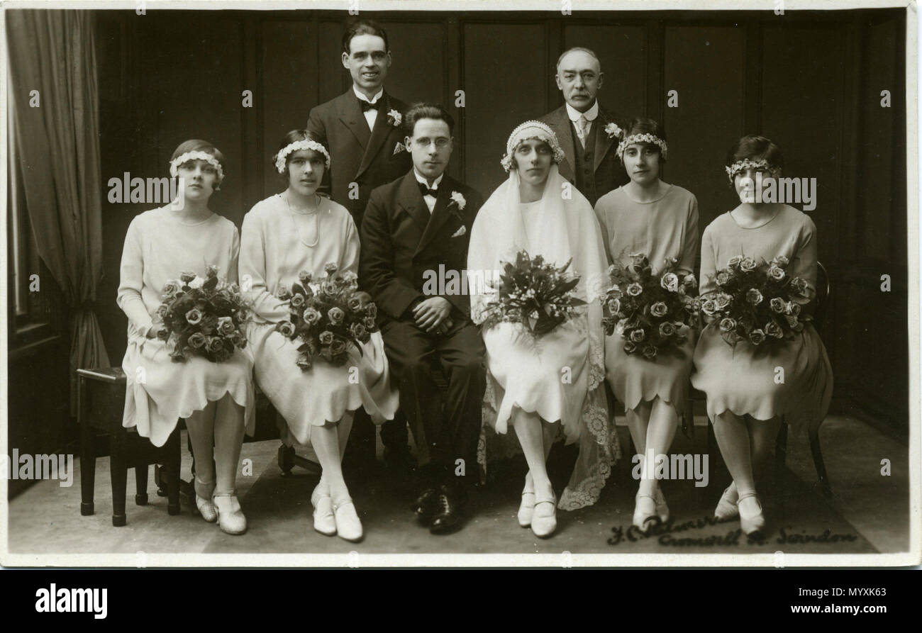 . 1920s or 1930s portrait photo of wedding group at Swindon, Wiltshire, England. The back of the card has the handwritten message: 'From Charlie & Edna, Salisbury', so it is understood that Charlie and Edna are the groom and bride. The photographer was Fred C. Palmer of Tower Studio, Herne Bay, Kent ca.1905-1920, and of 6 Cromwell Street, Swindon ca.1920-1936. He is believed to have died 1936-1939. Points of interest  The sepia print shows variation of tone in the bridesmaids' hand-made dresses, so it can be assumed that they are in various pastel colours. The men's suits and the ladies' silk  Stock Photo