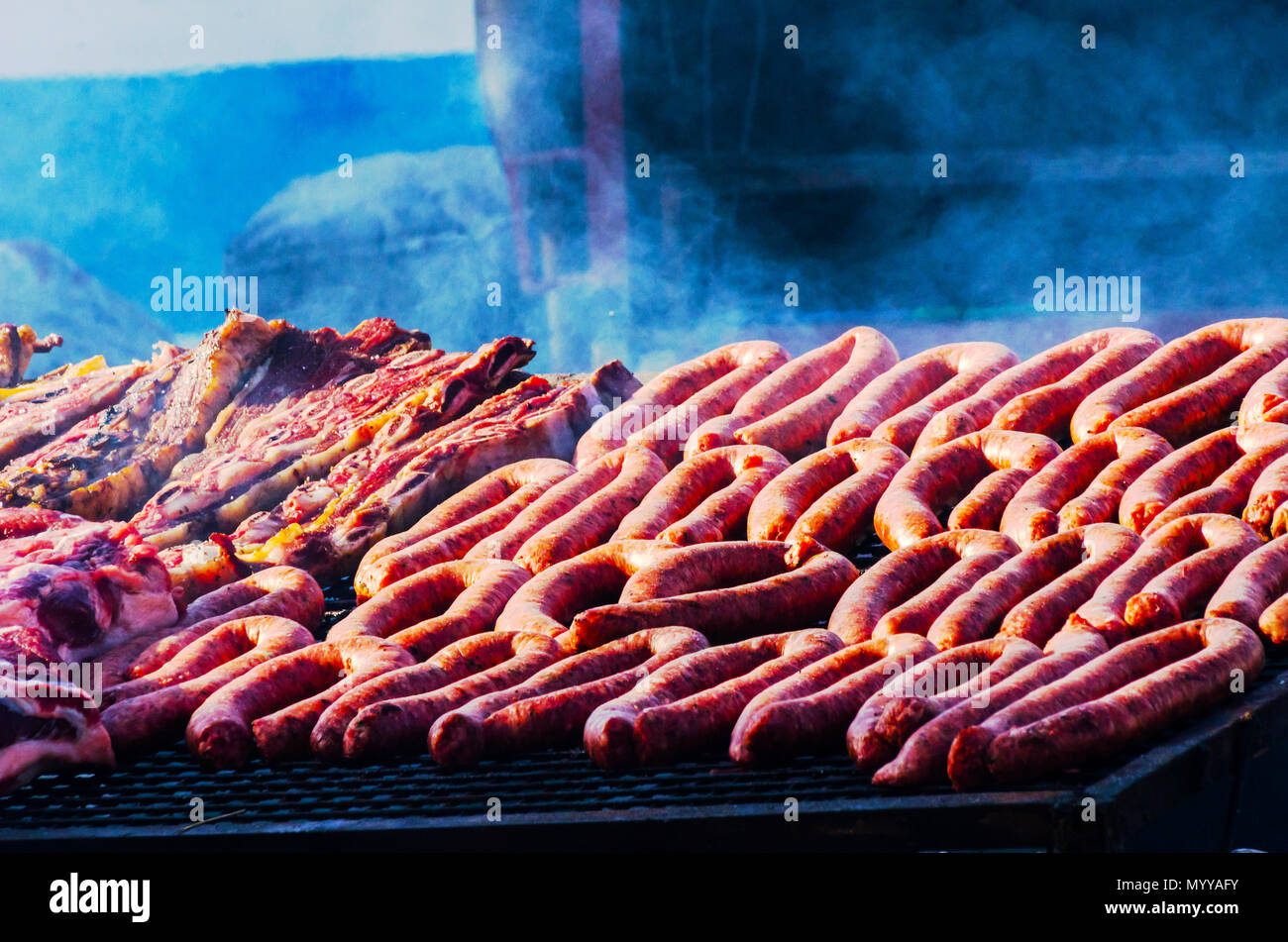 different types of meats and sausages stacked on a big grill while