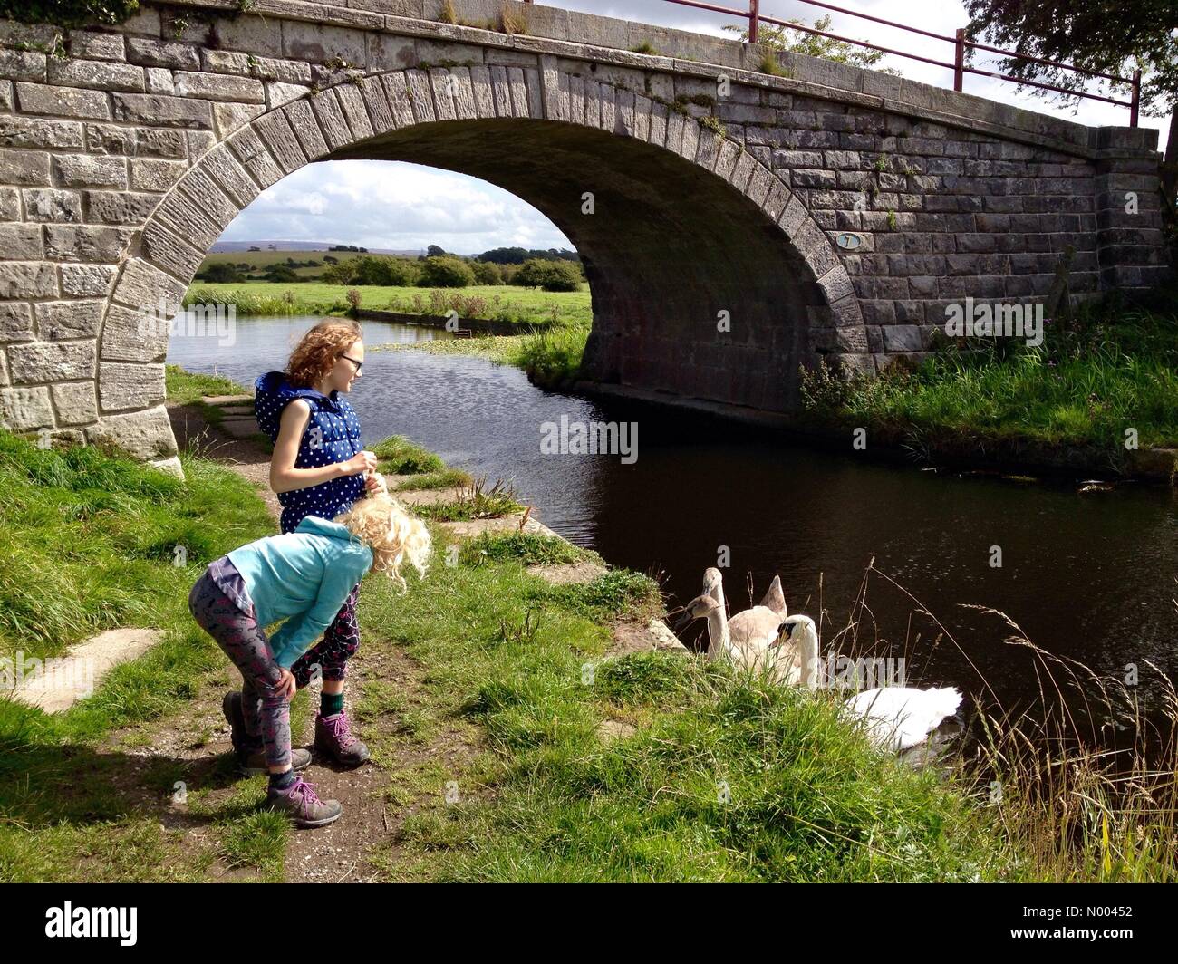 UK Weather sunny but windy at Glasson Dock near Lancaster in Lancashire. Two young girls looking at swans on Lancaster canal. Stock Photo