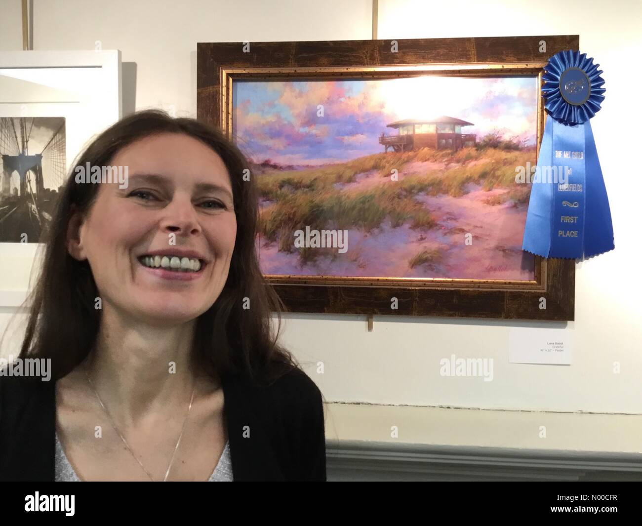 Port Washington Blvd, Manhasset, New York, USA. 07th Apr, 2017. LANA BALLOT, of Lake Grove, laughs next to her pastel painting of beach scene&quot;Grateful&quot; the First Place Winner of The Art Guild of Elderfields &quot;America!&quot; juried Art Show in Long Island Gold Coast. Credit: aparry/StockimoNews/Alamy Live News Stock Photo