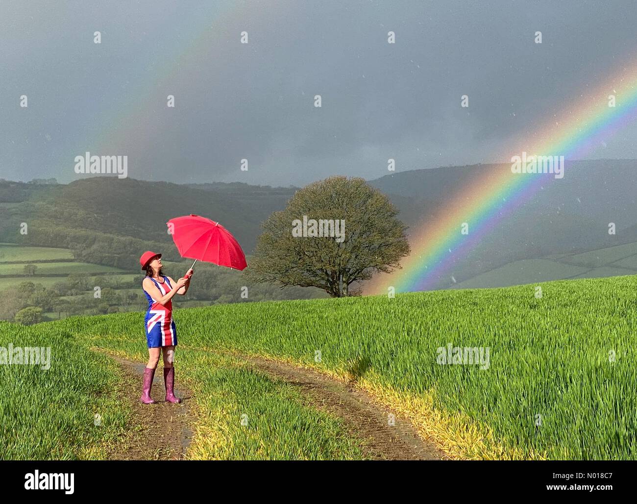 UK Weather: Raich Keene in Union Jack dress under a Colourful Rainbow in changeable conditions for Coronation weekend at Dunsford in Devon, UK. 5 May, 2023. Credit nidpor/ Alamy Live News Credit: nidpor/StockimoNews/Alamy Live News Stock Photo
