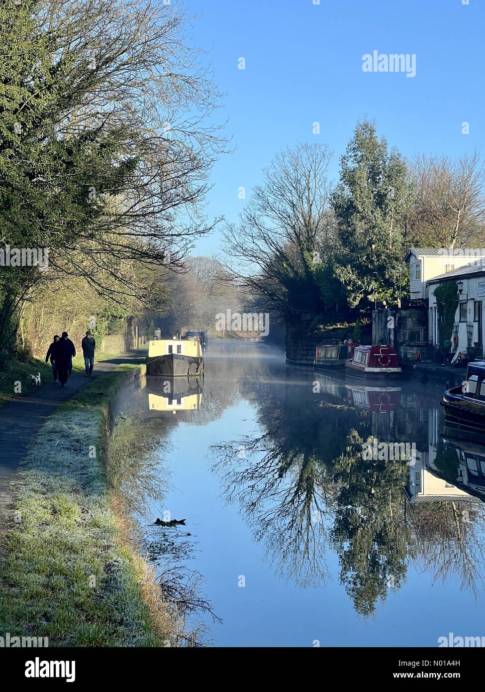 UK Weather: sunny and frosty in Adlington. Reflections of narrow boats on Leeds And Liverpool canal at Adlington in Lancashire with people walking on tow path Stock Photo