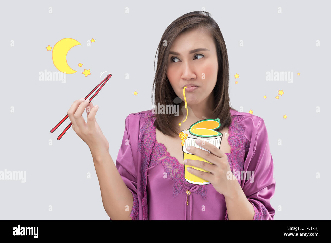 Asian woman in satin purple nightwear eating cup noodle at night. Female hungry at night on a gray background. Instant noodle. Stock Photo