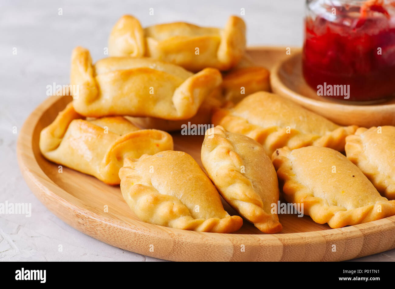 Two types of empanadas on a wooden plate with ketchup. White stone