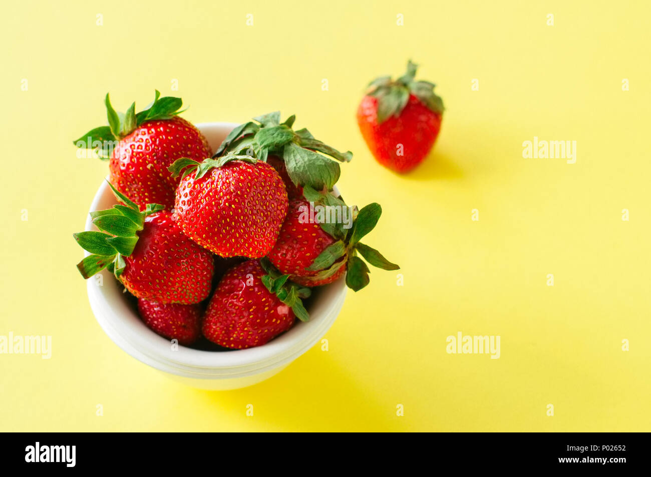 Heap of fresh ripe strawberries in a white bowl on a yellow background ...
