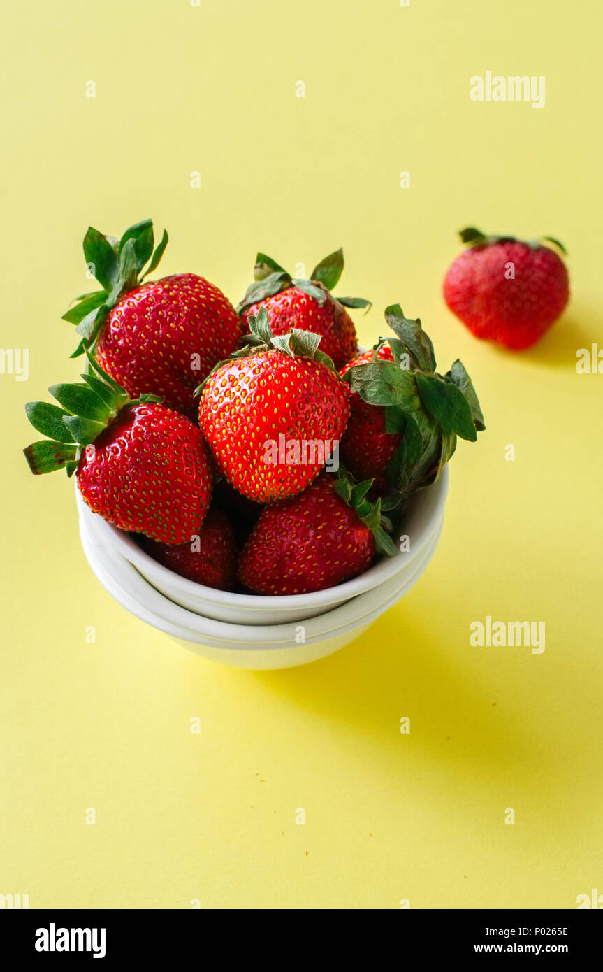 Heap of fresh ripe strawberries in a white bowl on a yellow background ...
