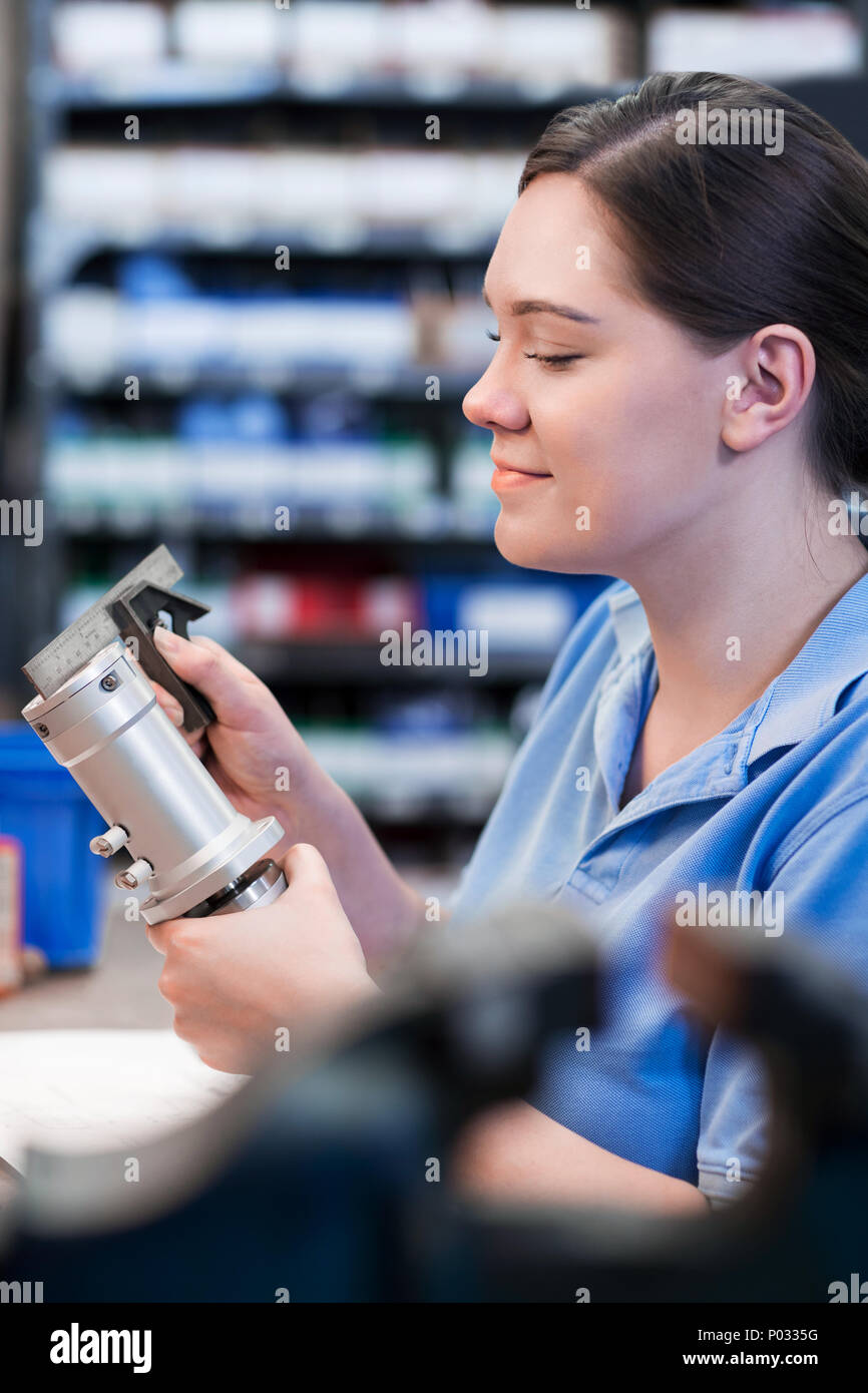 Female Apprentice Measuring Component In Factory Stock Photo