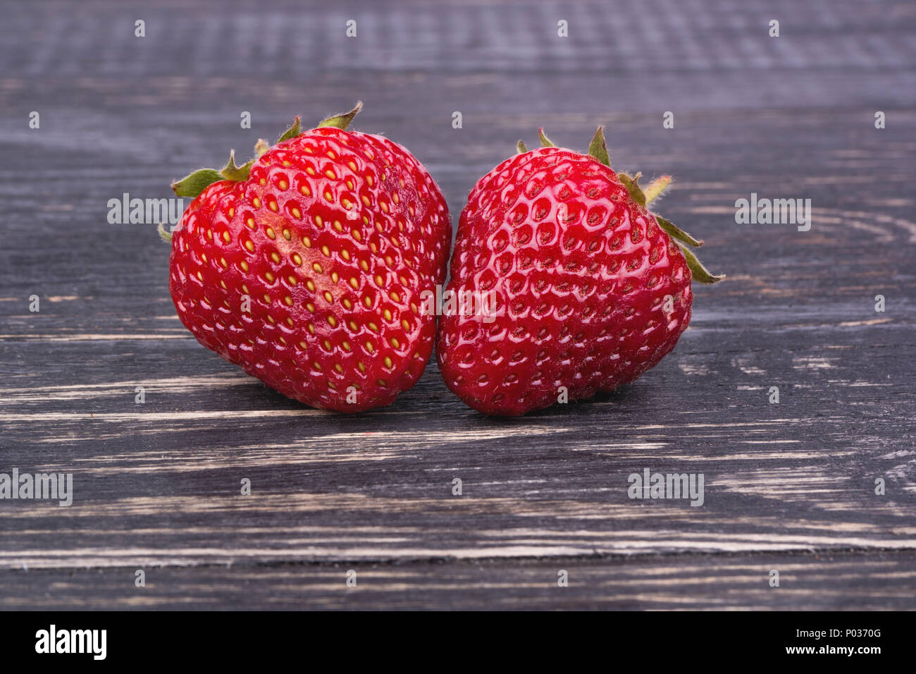 Two fresh ripe strawberries on a dark wooden background Stock Photo - Alamy