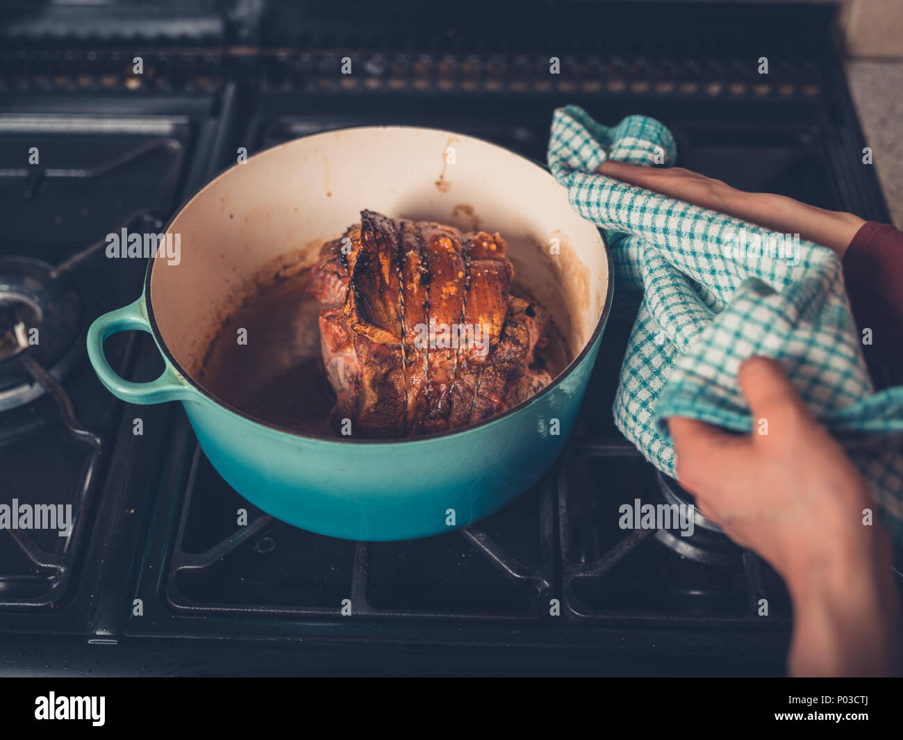 The hands of a young woman is handling a pot with a suculent and delicious pork roast Stock Photo