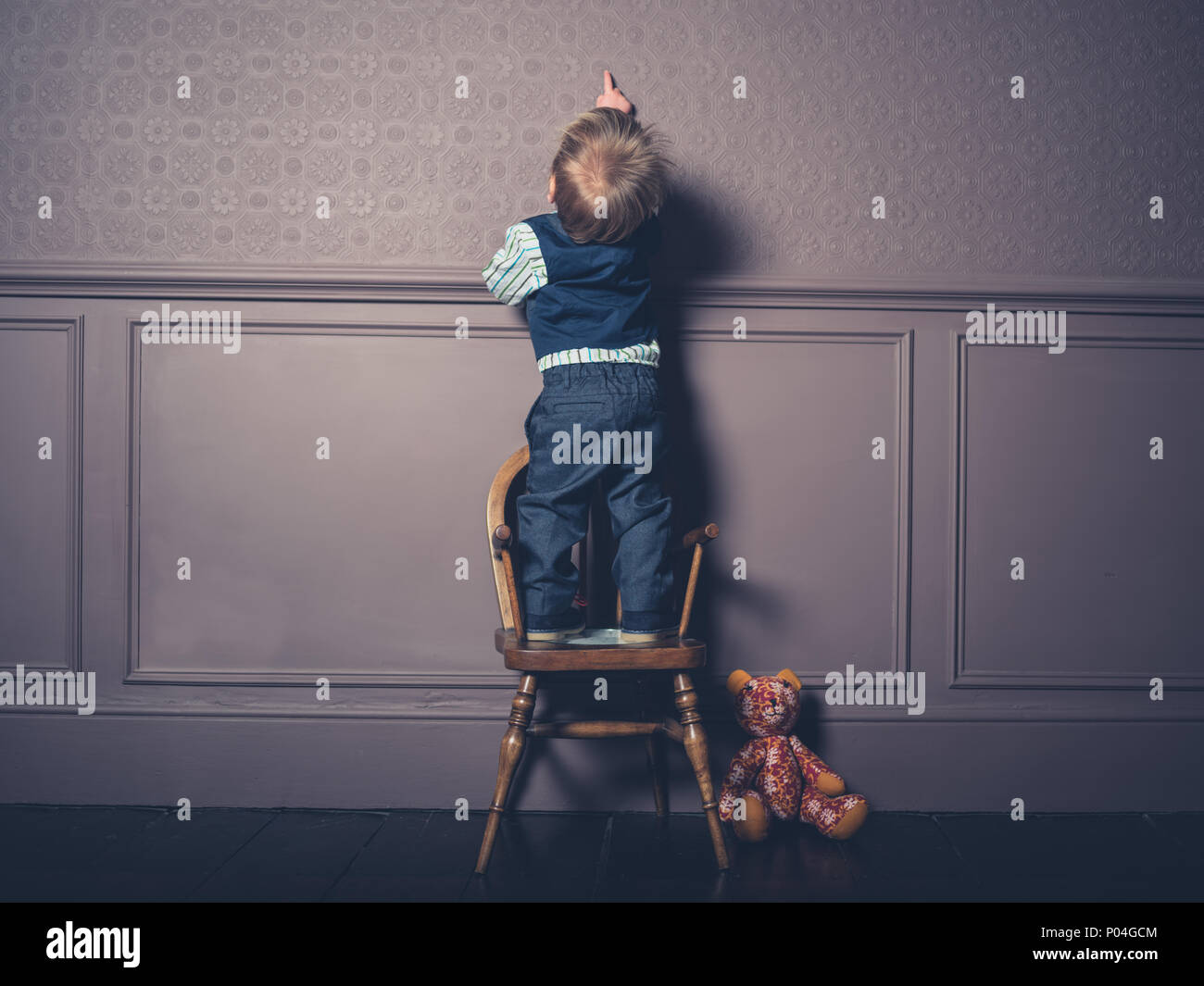 A cute little boy is standing on a chair in a luxury living room Stock Photo