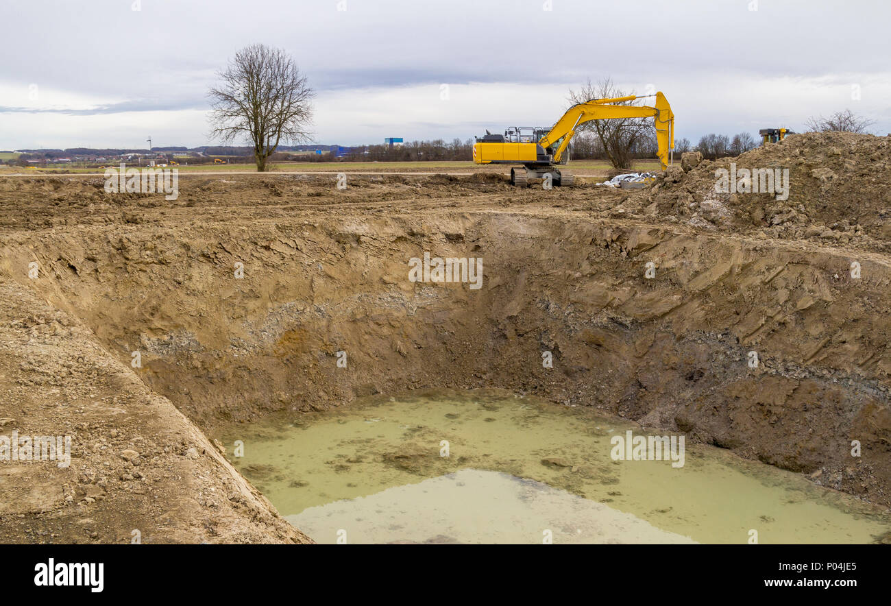 excavator at a big hole near a loamy construction site Stock Photo - Alamy