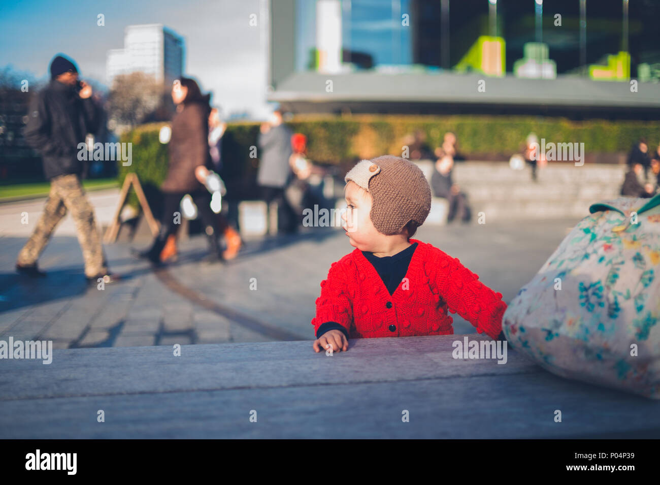 A little baby is standing in the city with crowds of people walking
