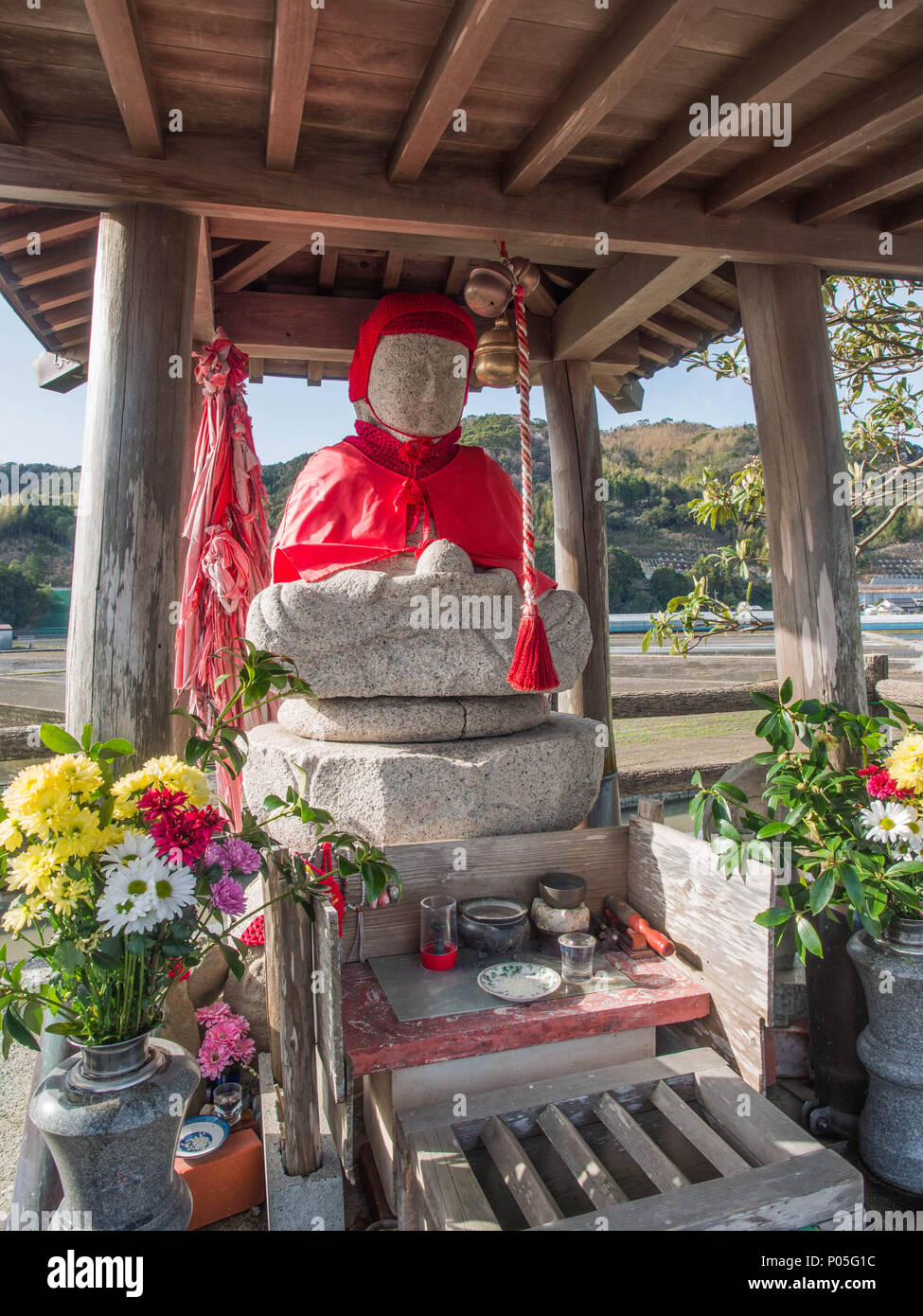 Roadside shrine, henro no michi pilgrim trail, Jizo Bosatsu statue in red robes, with offerings, Kochi, Shikoku, Japan Stock Photo