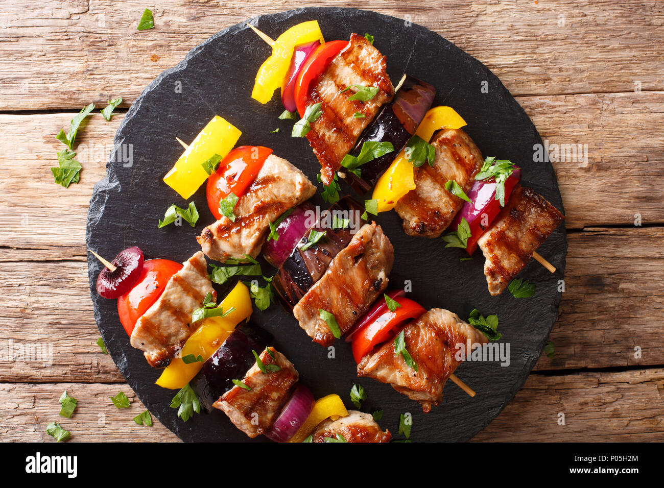 Juicy grilled kebabs of pork with tomatoes, pepper, onions and eggplants close-up on a slate plate on a table. horizontal top view from above Stock Photo