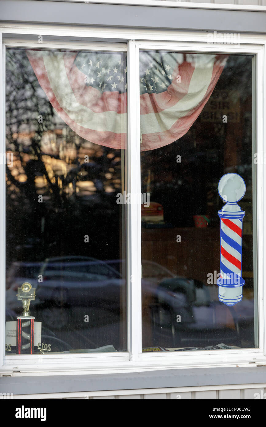 Johnstown, New York: Barbershop window displays traditional barbers pole, flag bunting and a trophy. Stock Photo