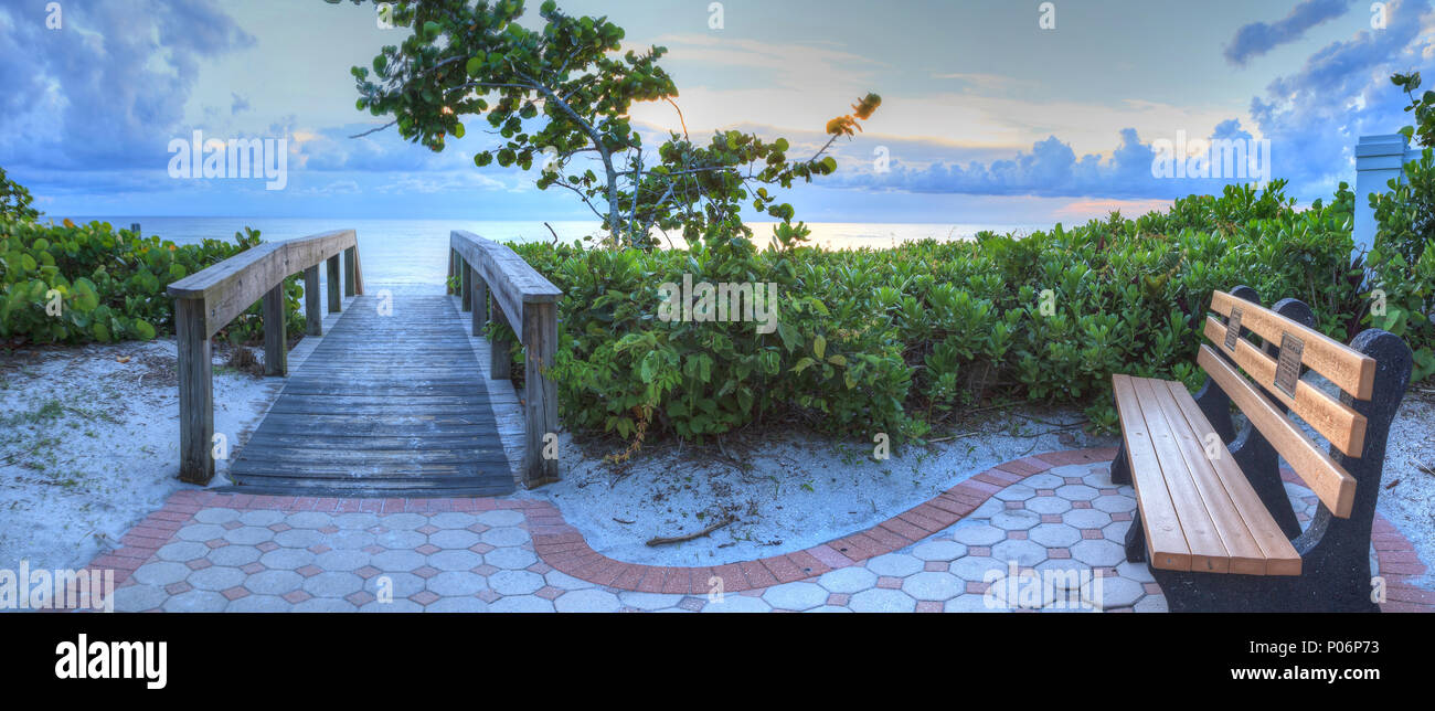 Bench overlooks a wooden boardwalk onto Naples Beach at sunset in Naples, Florida. Stock Photo