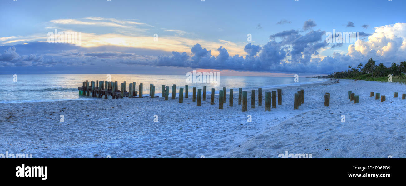 Sunset over Old pier at the ocean on Naples Beach with dark skies overhead and rain on the horizon in Naples, Florida Stock Photo