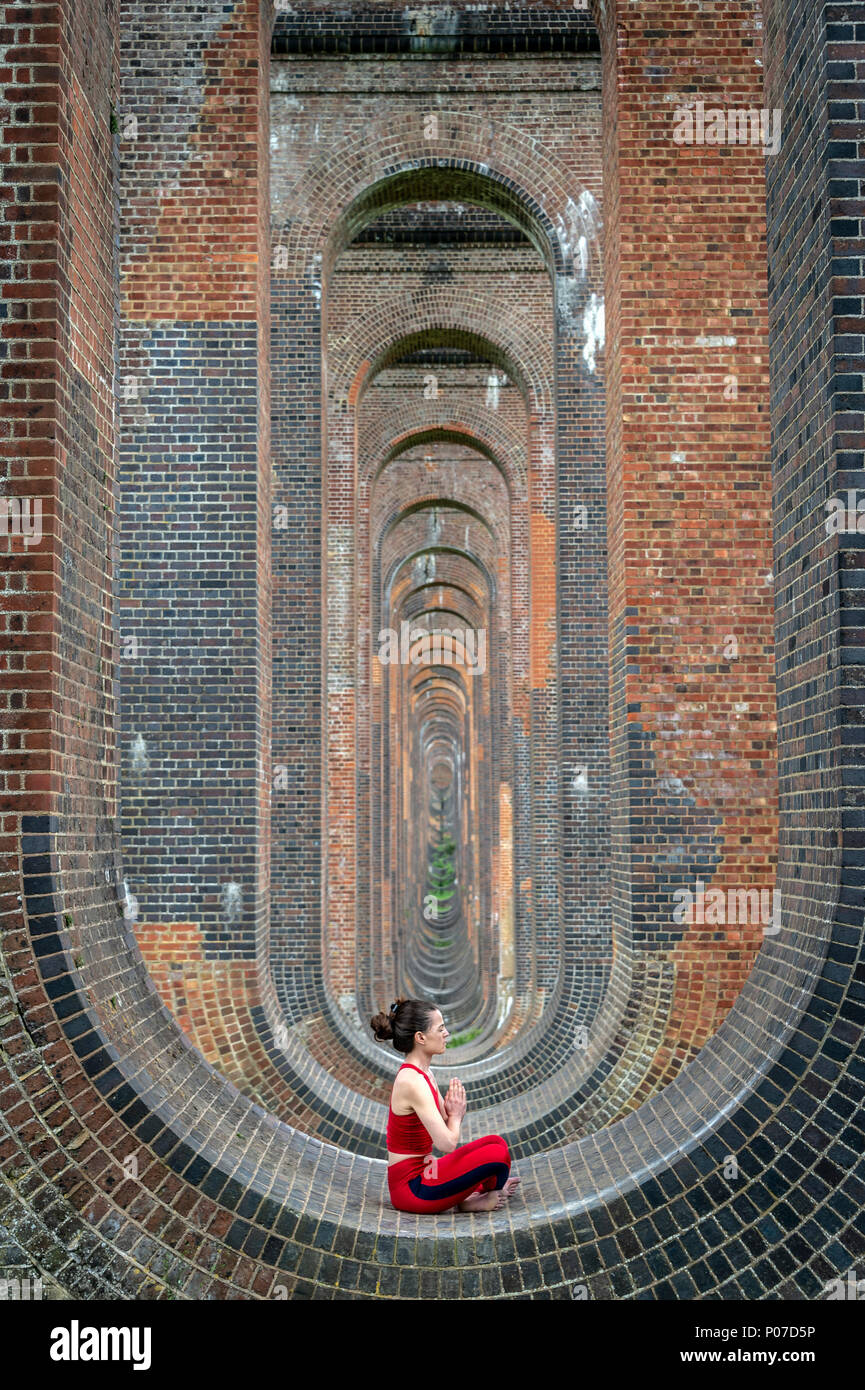 woman sitting in the arches of the Ouse Valley Viaduct practicing yoga and meditating Stock Photo