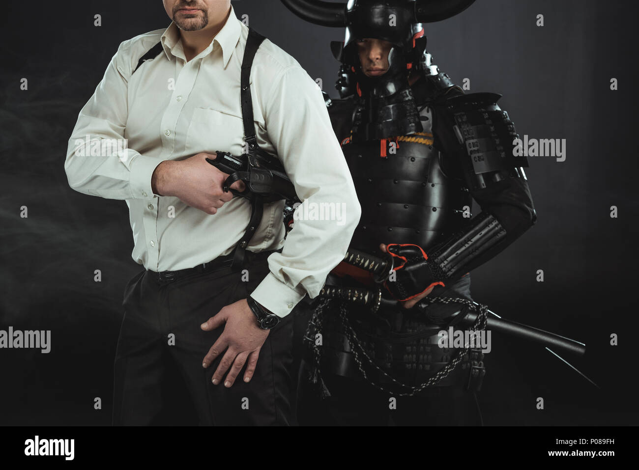cropped shot of man with gun and samurai behind him on black Stock ...