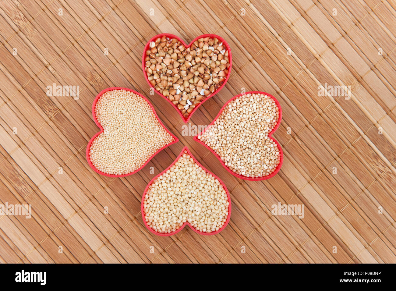 Gluten-free super seeds millet, buckwheat, amaranth and quinoa in red hearts on bamboo Stock Photo