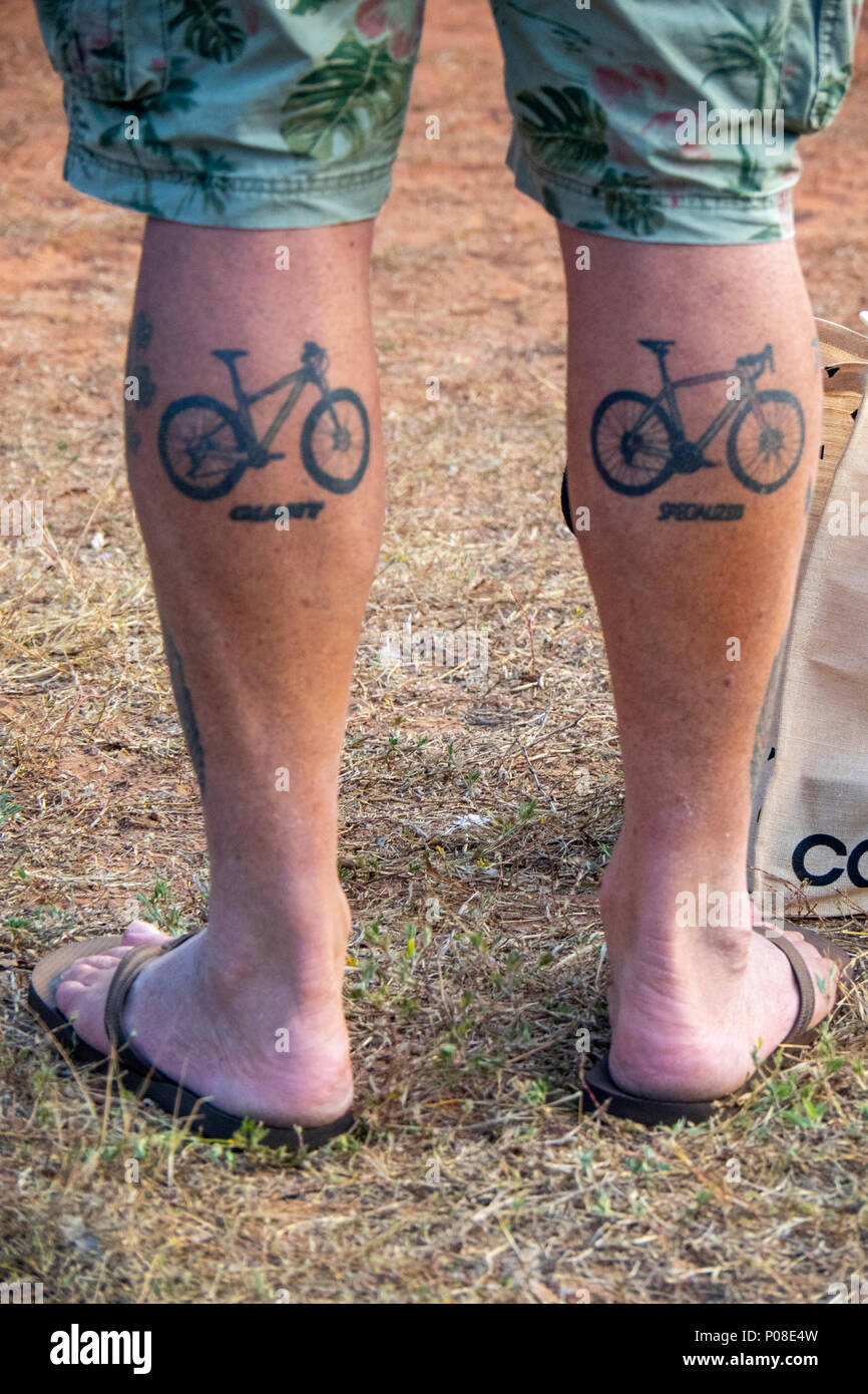 A man's calf muscles tattooed with a Giant Bike and a Specialized Bicycle Stock Photo - Alamy