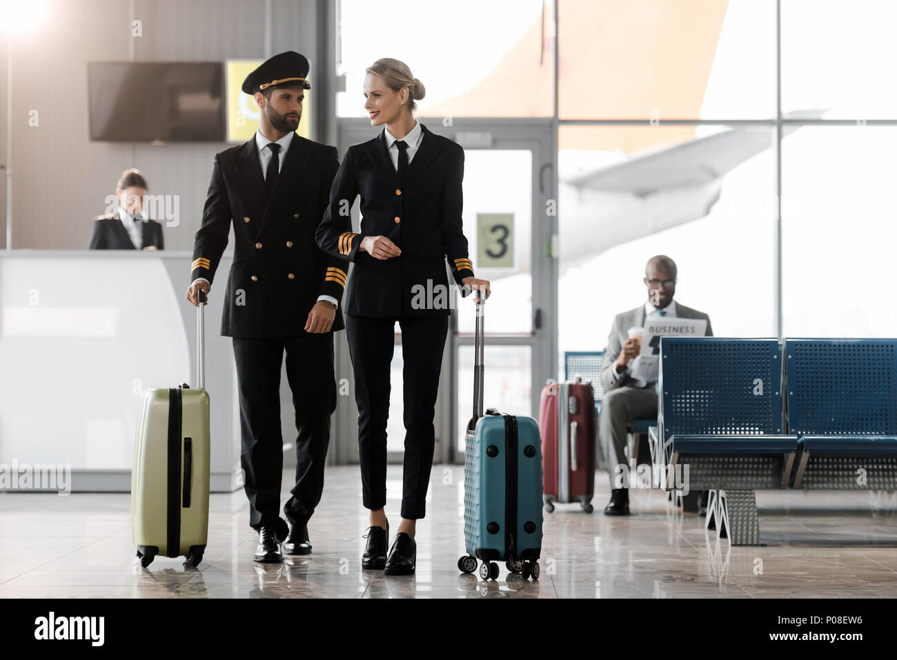 male and female pilots walking by airport lobby with suitcases Stock