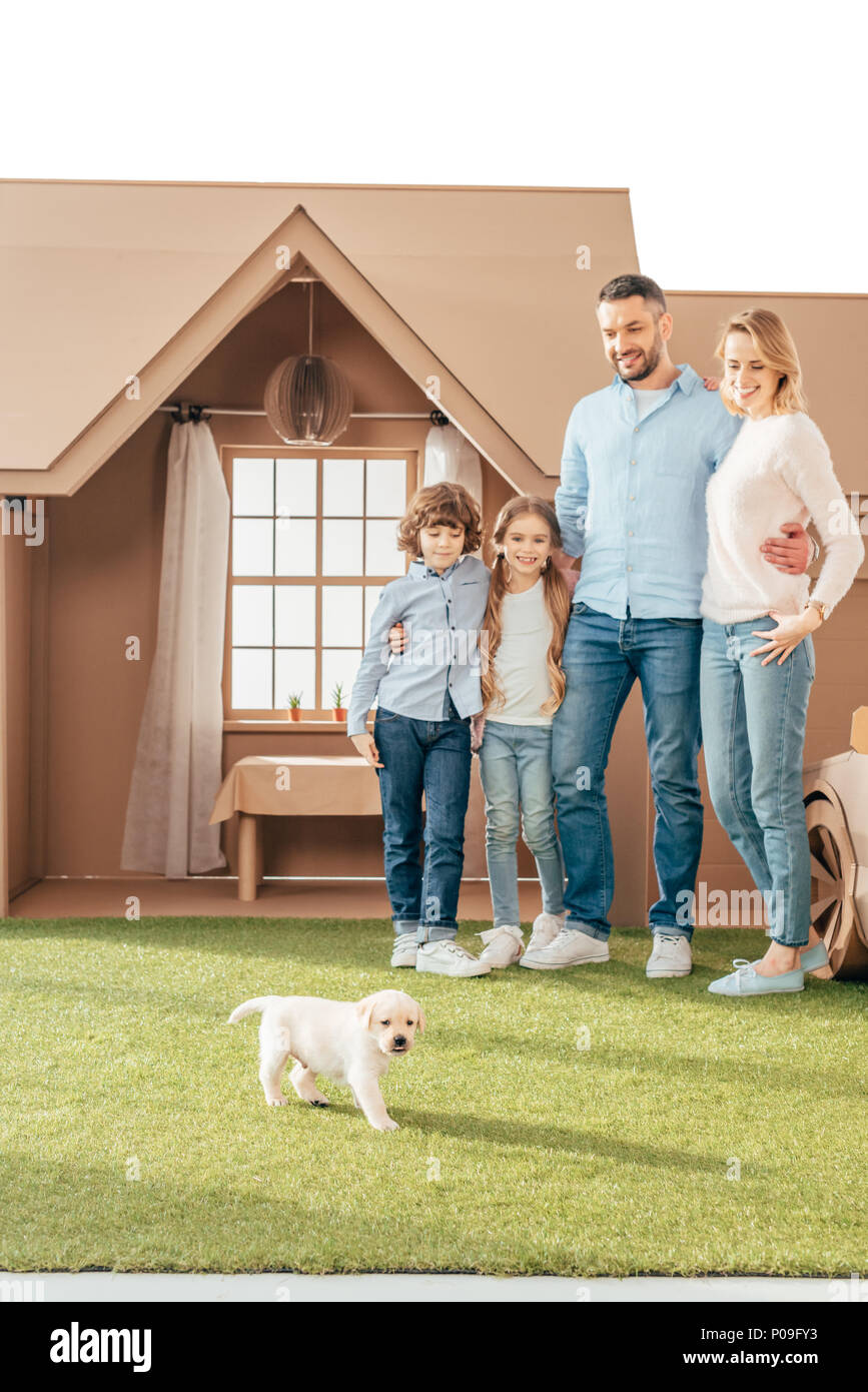 happy young family with adorable puppy on yard of cardboard house isolated on white Stock Photo