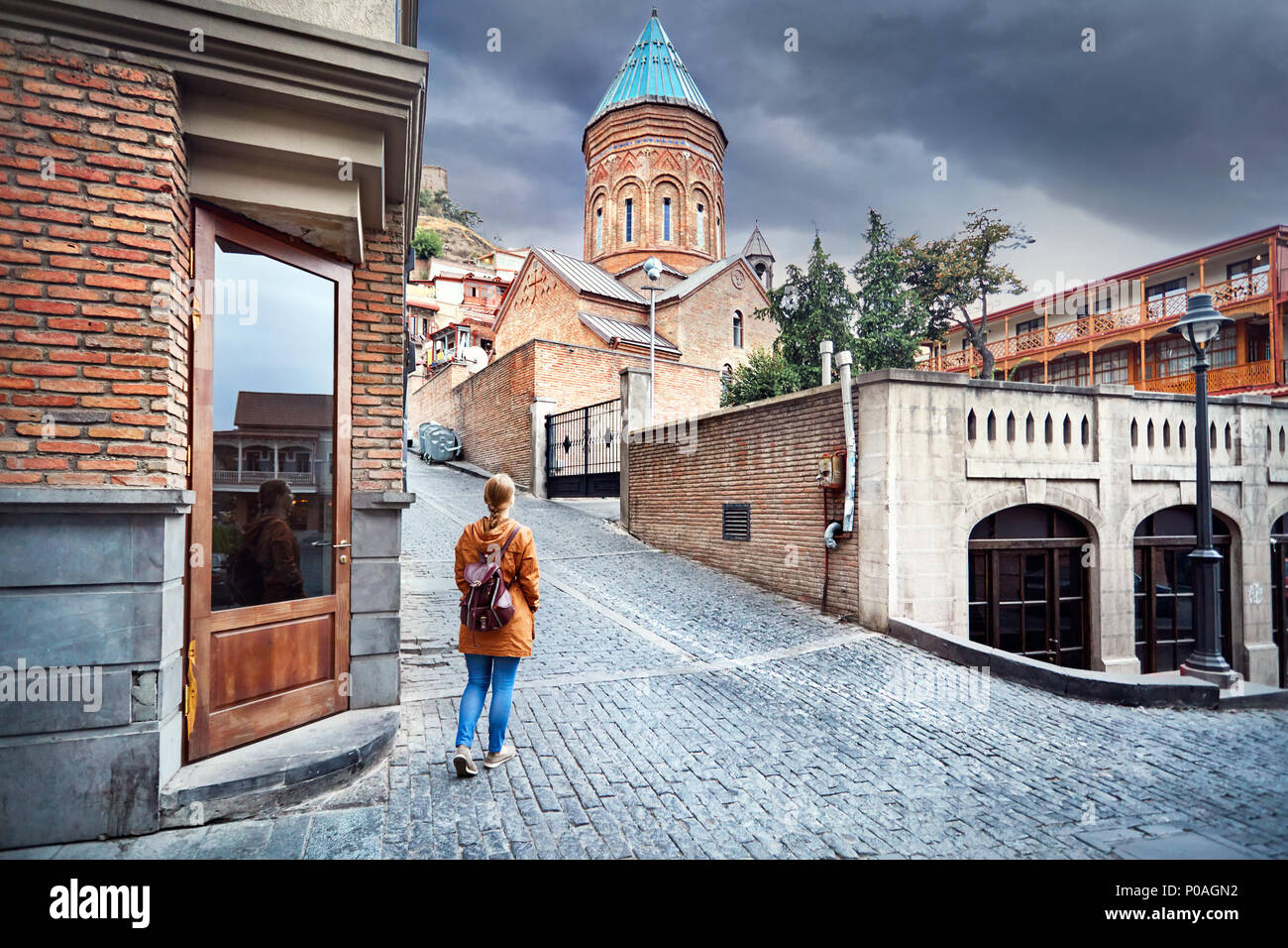 Tourist woman in brown jacket walking down the Old streets near church in central Tbilisi, Georgia Stock Photo