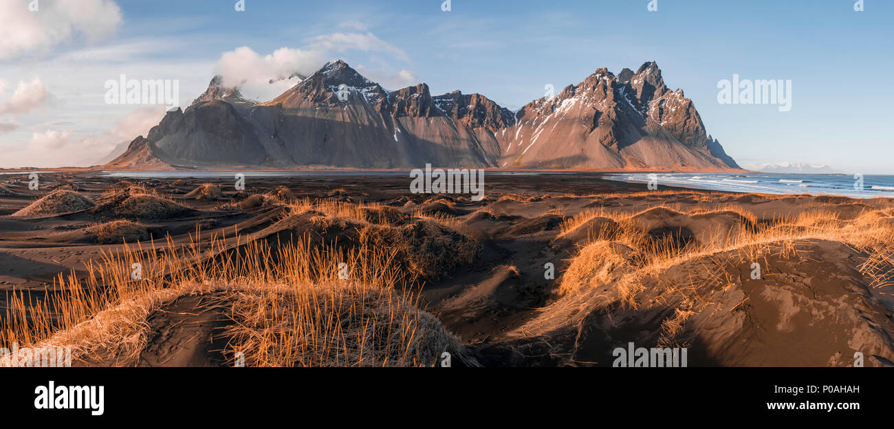 Evening atmosphere at the long lava beach, black sandy beach, dunes covered with dry grass, mountains Klifatindur Stock Photo