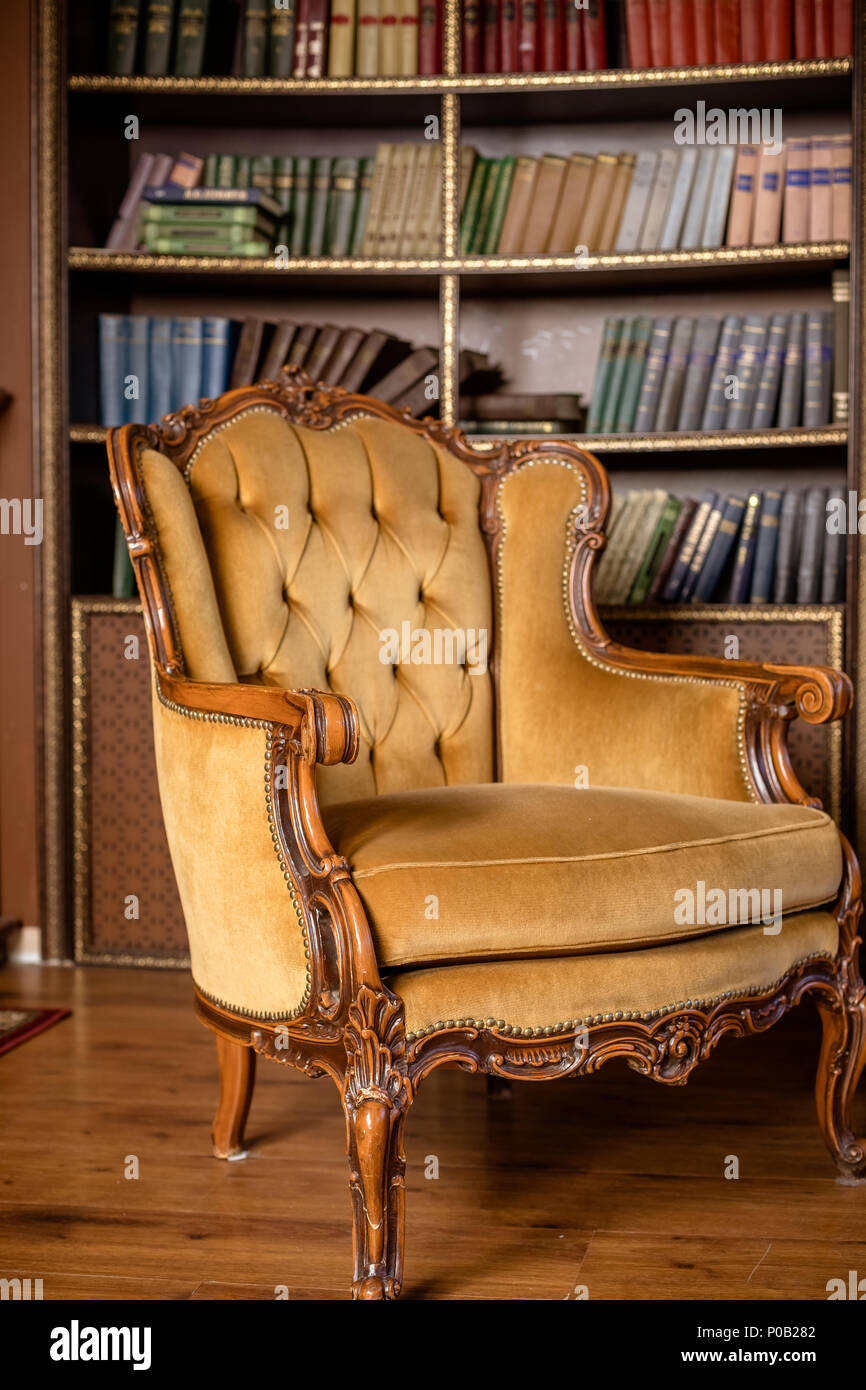 Books on bookshelves. Luxury yellow armchair in library room.Still Life