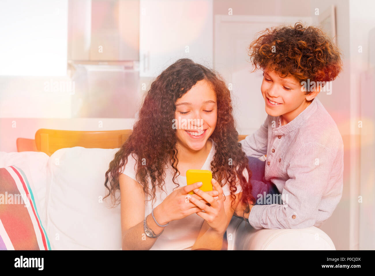 Cute curly teenage girl and boy chatting using cell phone indoors Stock Photo