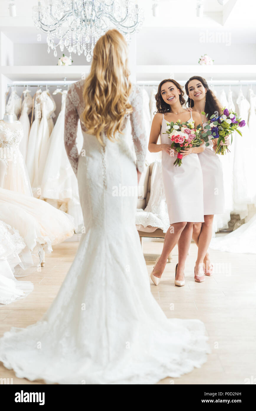 Bridesmaids with flowers looking at beautiful bride in wedding atelier ...